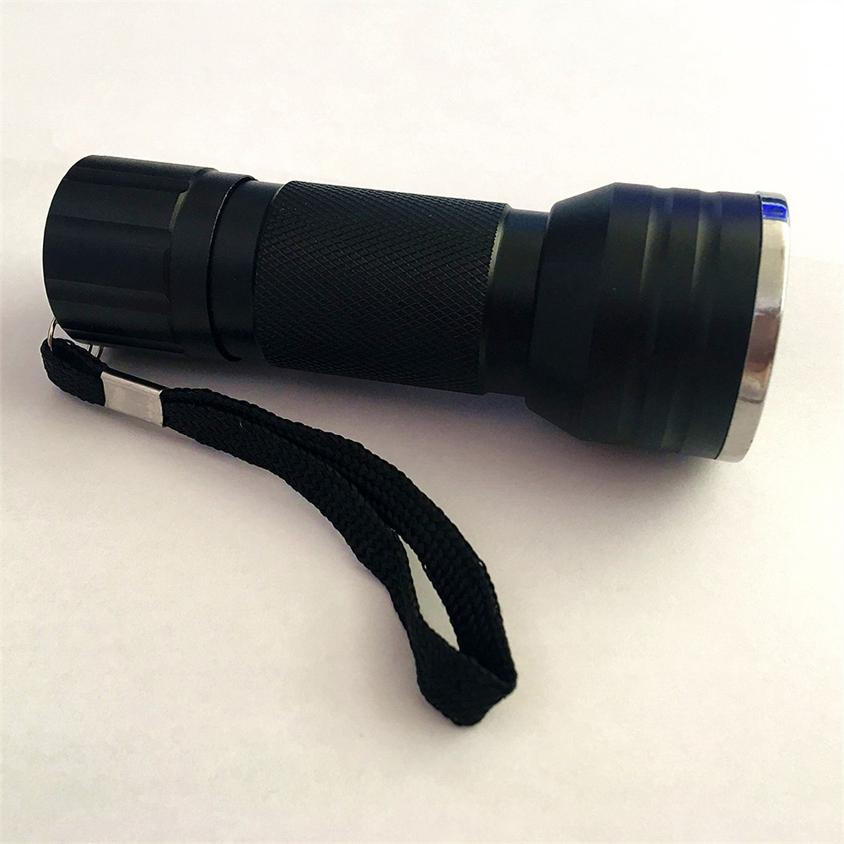 Eine schwarze Taschenlampe mit schwarzem Handgelenkband liegt auf weißem Untergrund.