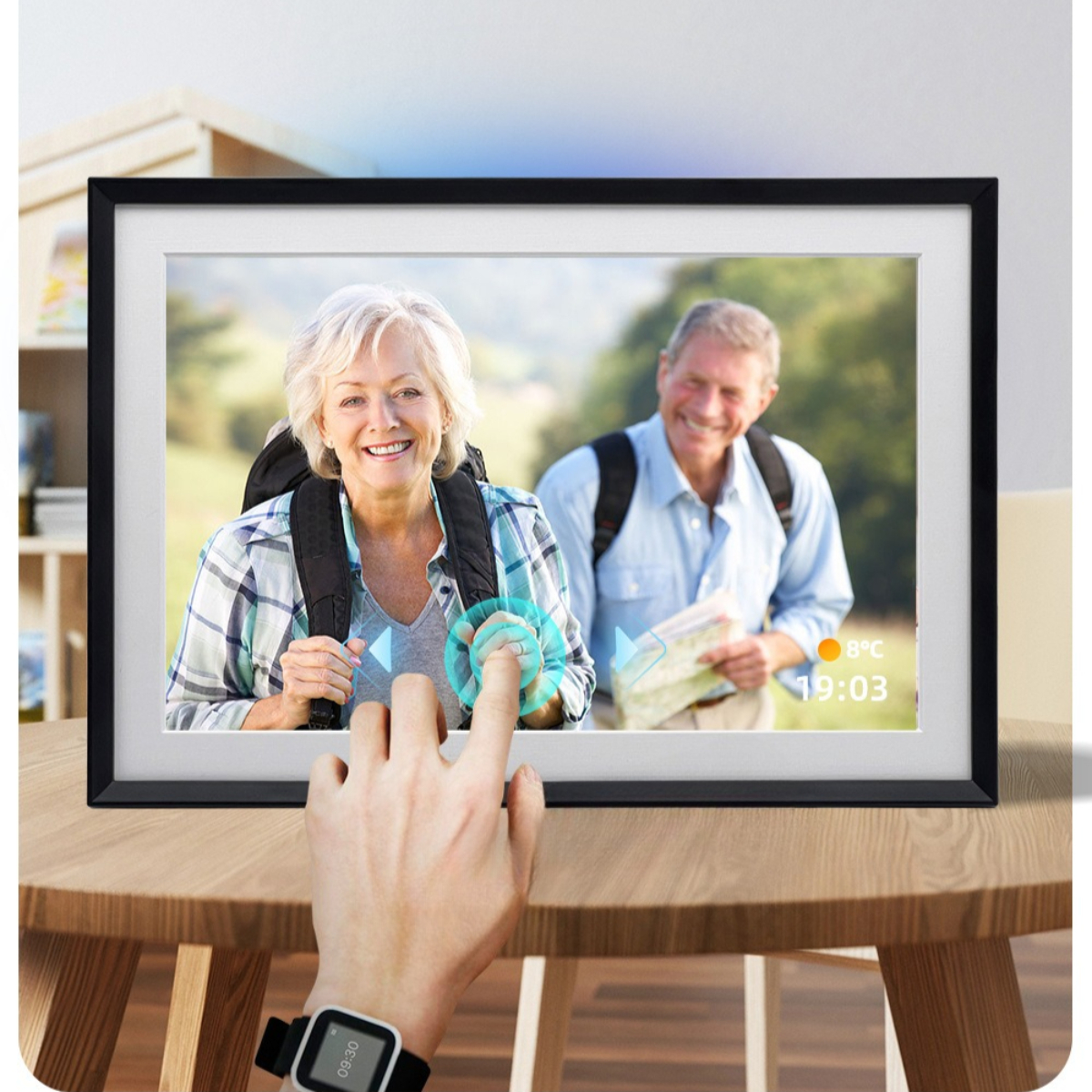 Digitaler Fotorahmen, der ein Paar anzeigt, wobei eine Person den Bildschirm berührt. Eine Smartwatch liegt auf einem Tisch.