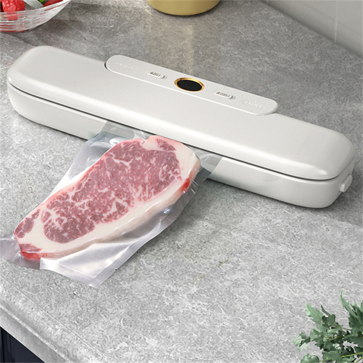 Weißes Vakuumiergerät mit einem Steak in einer Tüte auf einer grauen Arbeitsplatte. Inklusive Etikett.