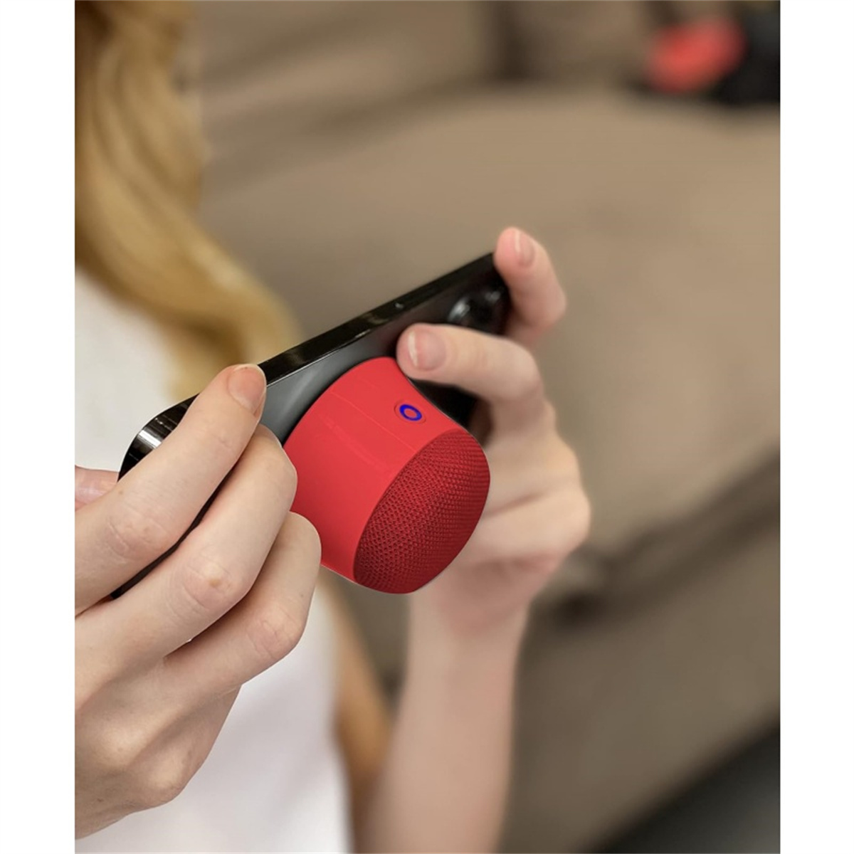 Ein kleiner roter Lautsprecher, der mit einem Telefon verbunden ist, das in Händen gehalten wird, mit einem blauen Licht auf dem Lautsprecher.