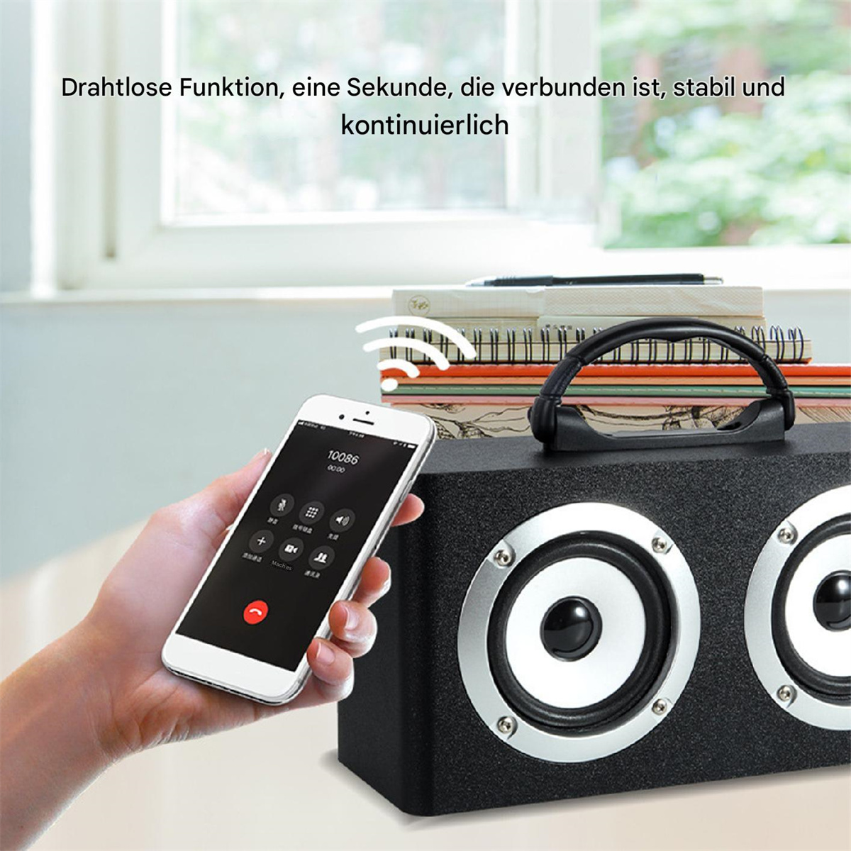 Eine Hand hält ein Telefon. Ein Lautsprecher steht auf einem Tisch. Der Telefonbildschirm zeigt einen Anrufbildschirm.