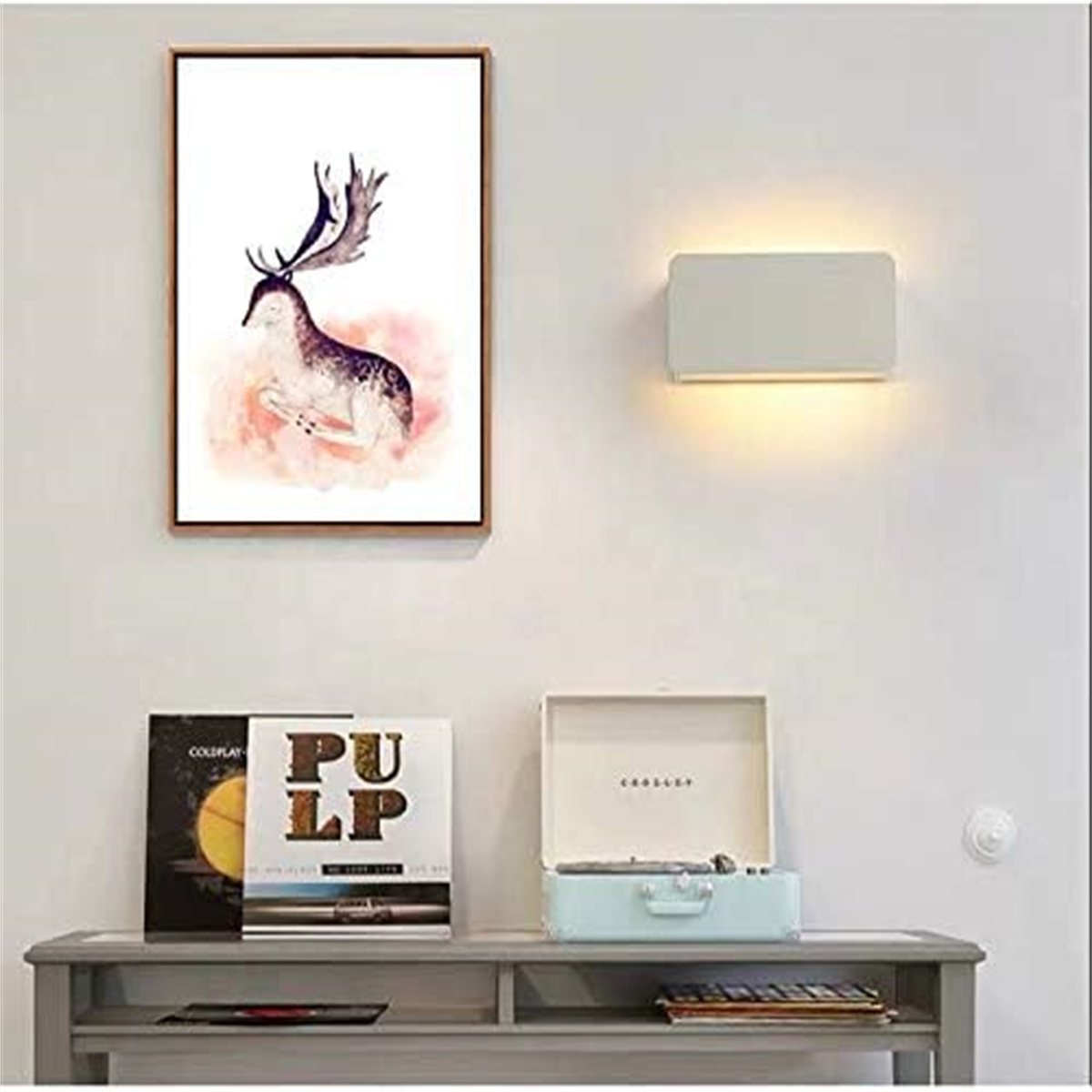 Ein Gemälde eines Hirsches, eine Wandlampe, ein Plattenspieler und Schallplatten an einer weißen Wand.