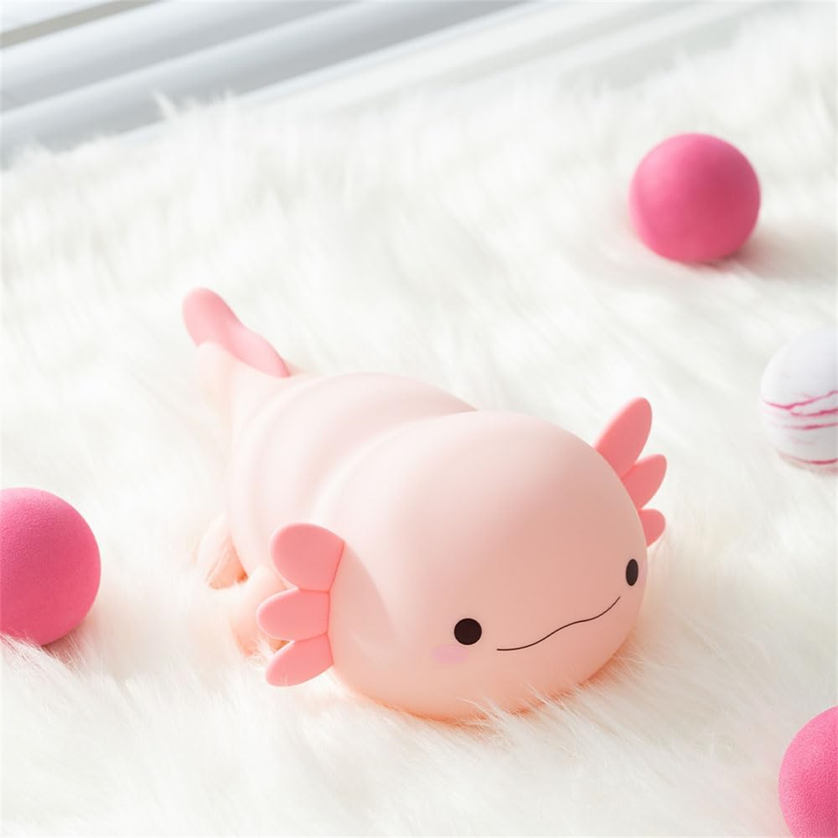 Rosa Axolotl-Spielzeug auf weißem Fell, mit rosa Bällen. Das Axolotl liegt.