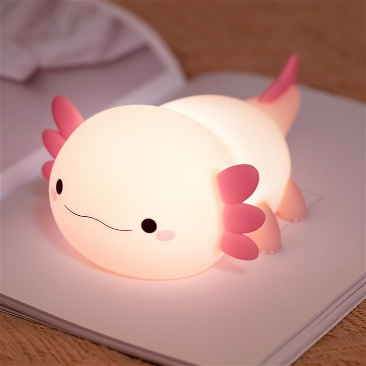 Axolotl-Nachtlicht, das sanft auf einem offenen Buch leuchtet. Rosa und weiß.