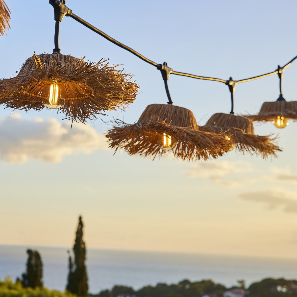 Stroh-Lampen vor einem Sonnenuntergangshimmel über dem Meer. Warme Beleuchtung.