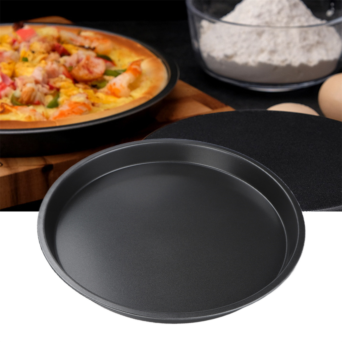 Eine schwarze Pizzapfanne mit einer Pizza darin, eine schwarze Platte daneben und Zutaten im Hintergrund.