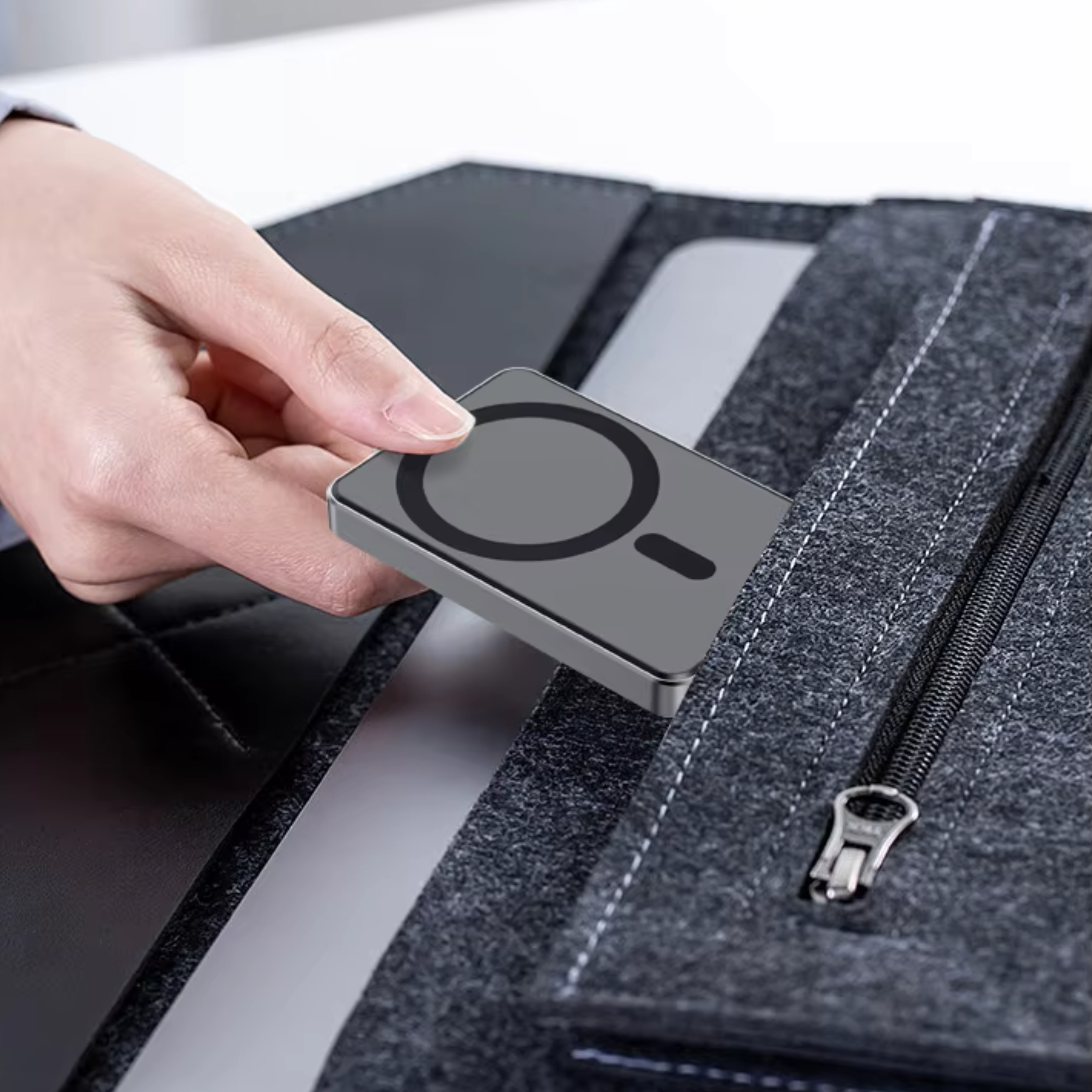 Hand, die ein graues Ladezubehör in eine schwarze Filztasche legt.