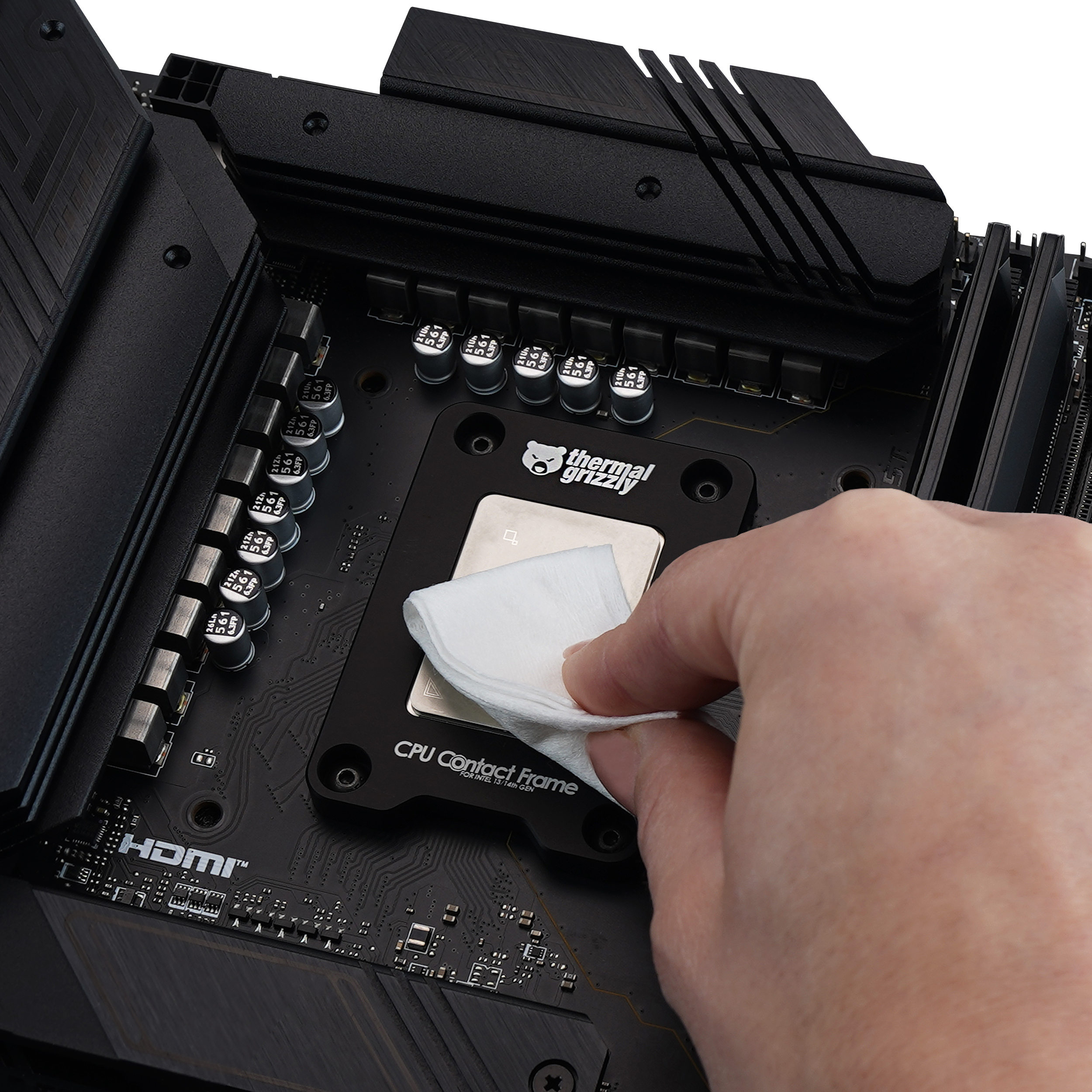 Une main nettoyant le CPU sur une carte mère avec un chiffon blanc. Composants noirs et argentés visibles.