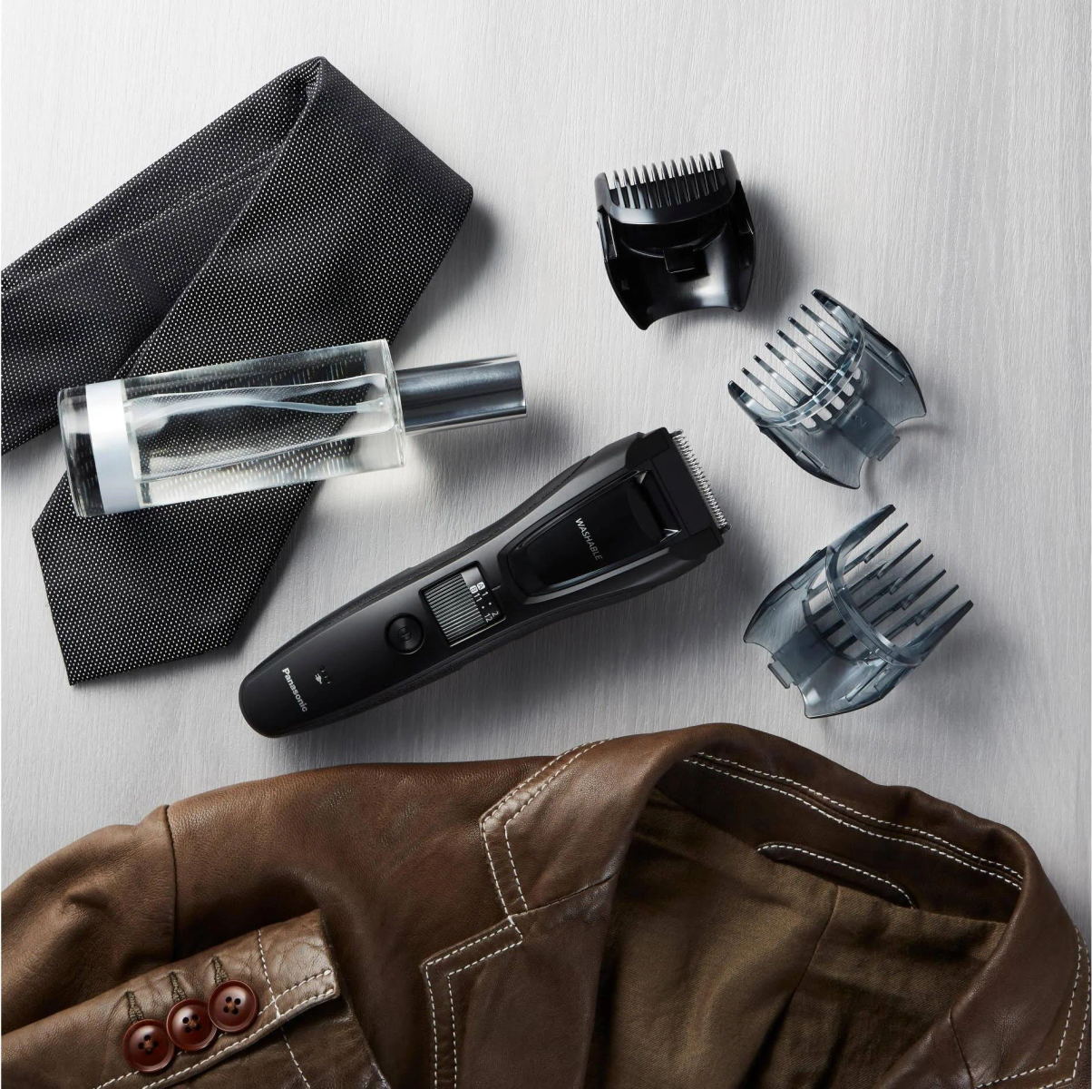 Set da uomo per la cura personale con trimmer nero, accessori, cravatta, giacca e colonia. Gli oggetti sono disposti.