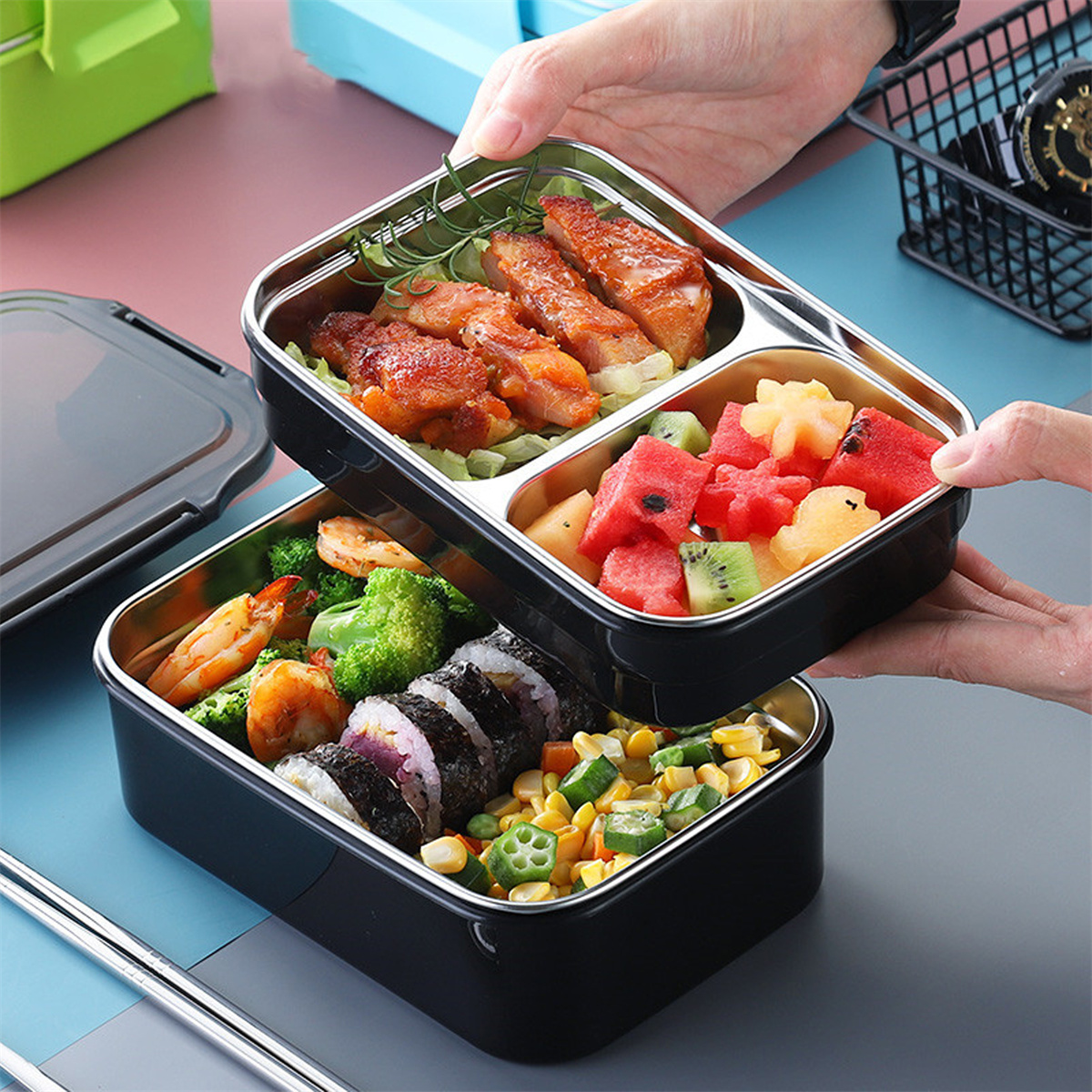 Lunchbox mit zwei Fächern. Enthält Lebensmittel wie Sushi, Hühnchen, Wassermelone und Brokkoli.