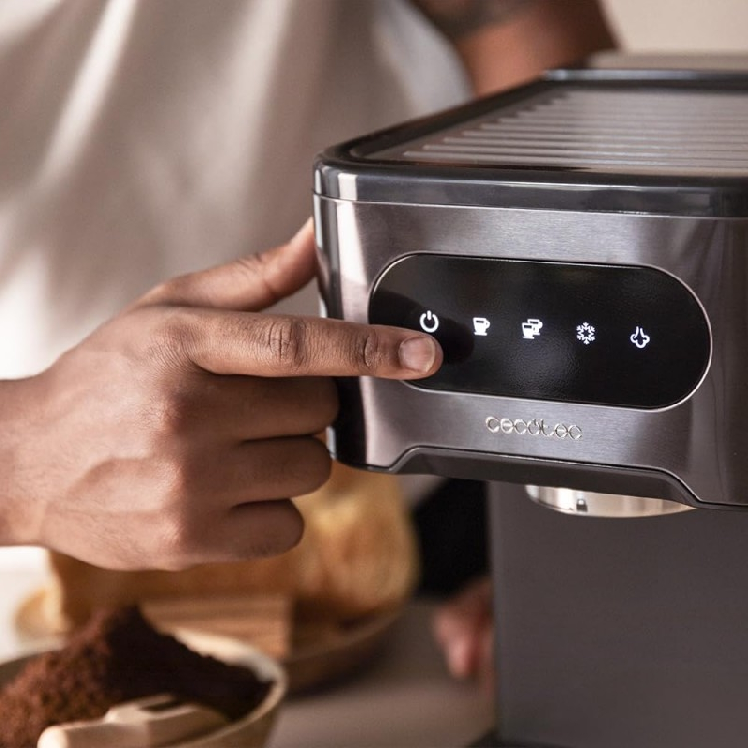 Dłoń naciska przycisk na czarno-srebrnym ekspresie do kawy. Widoczne ikony kawy.