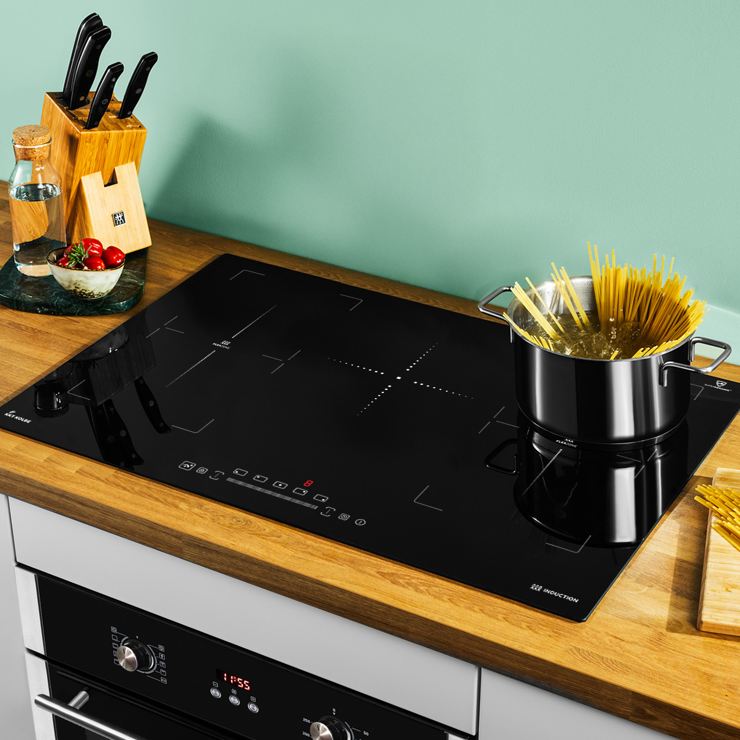 Schwarzes Induktionskochfeld mit Pasta in einem Topf, Gemüse und Utensilien auf einer Holztheke.