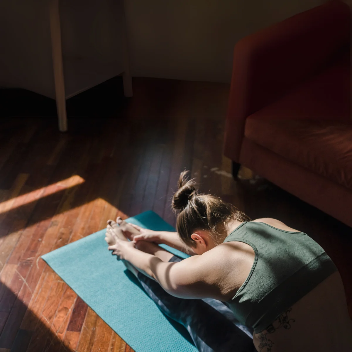 Vrouw die zich uitrekt op een yogamat op een houten vloer.