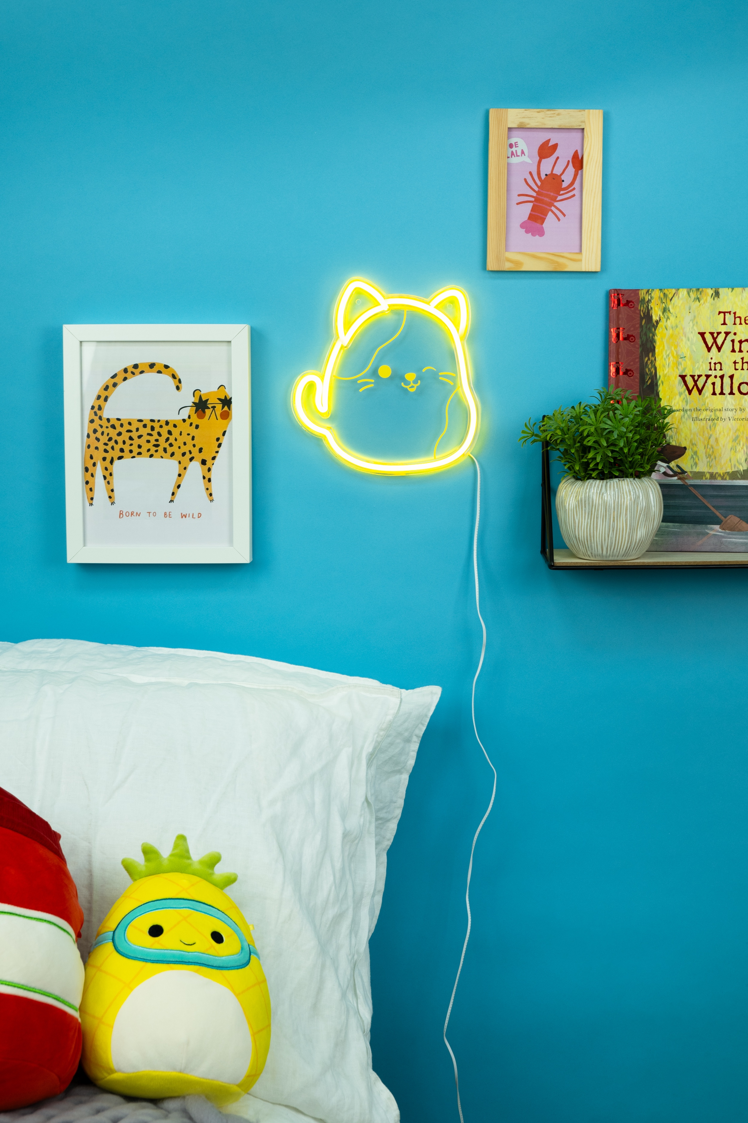 Een kamer met blauwe muren, een bed en foto's. Een neon kattenlicht staat op de muur.