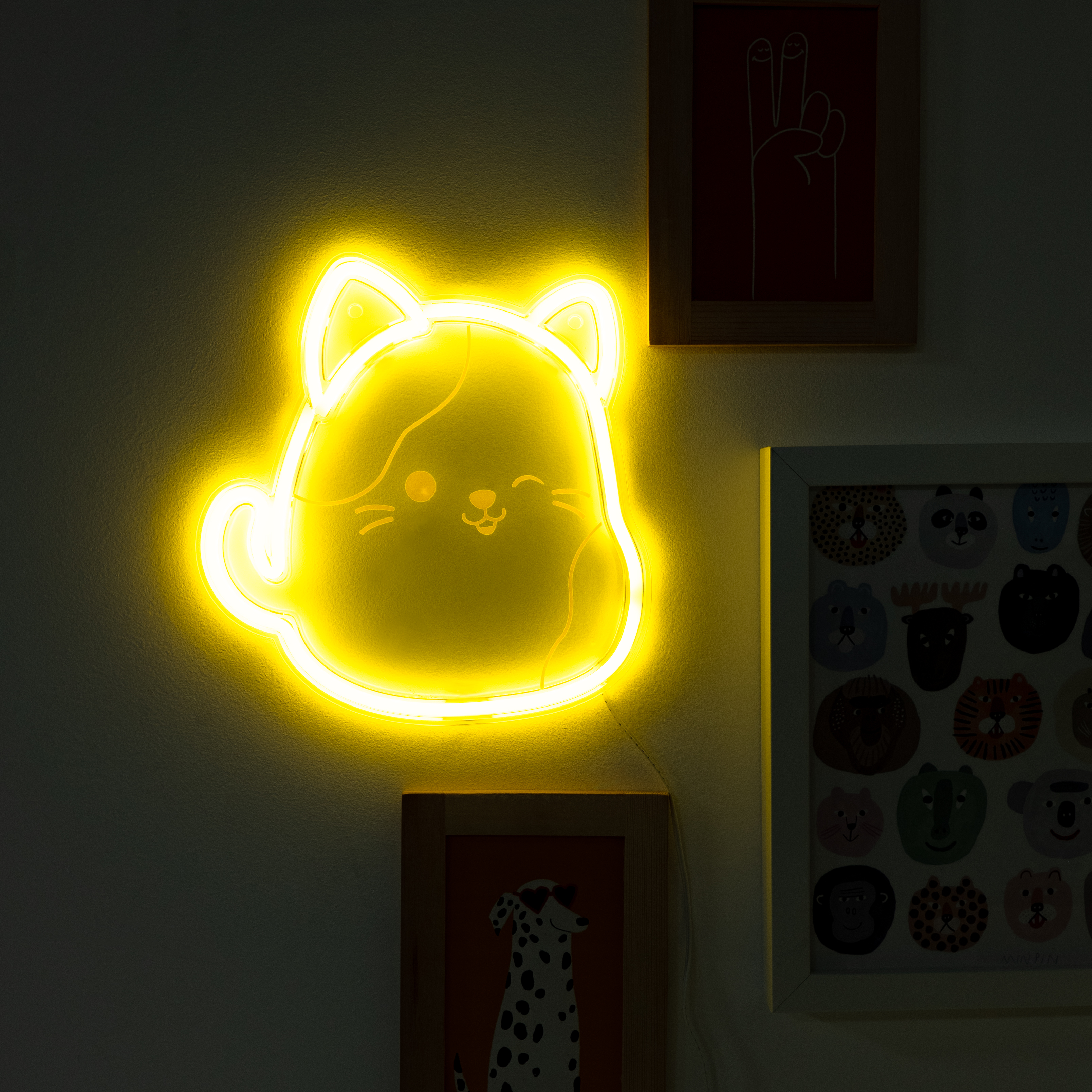 Een gele neonkatvormige lamp aan een muur, met ingelijste foto's in de buurt.