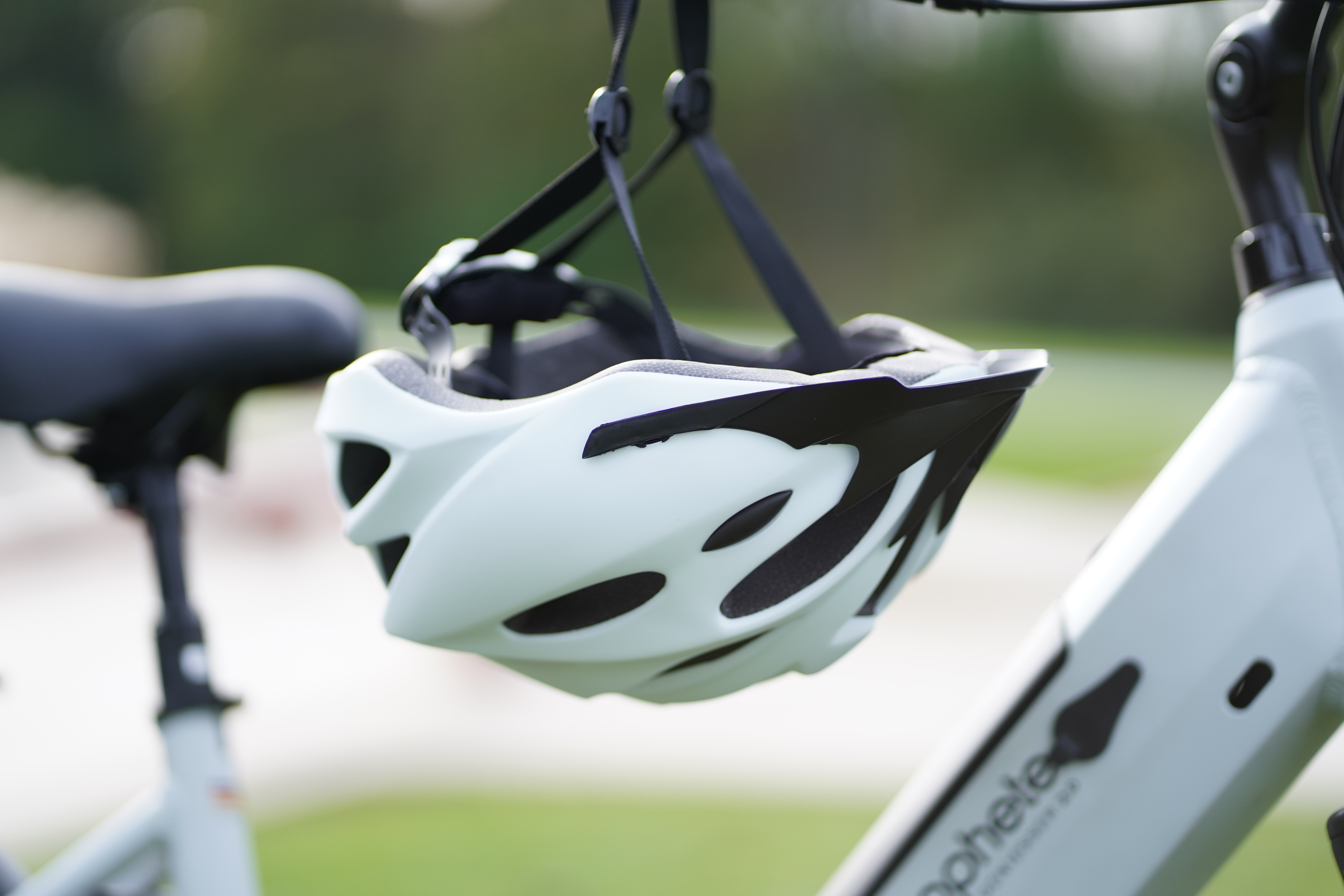 Ein grün-schwarzer Fahrradhelm, der am Lenker eines Fahrrads hängt. Der Hintergrund ist Gras.