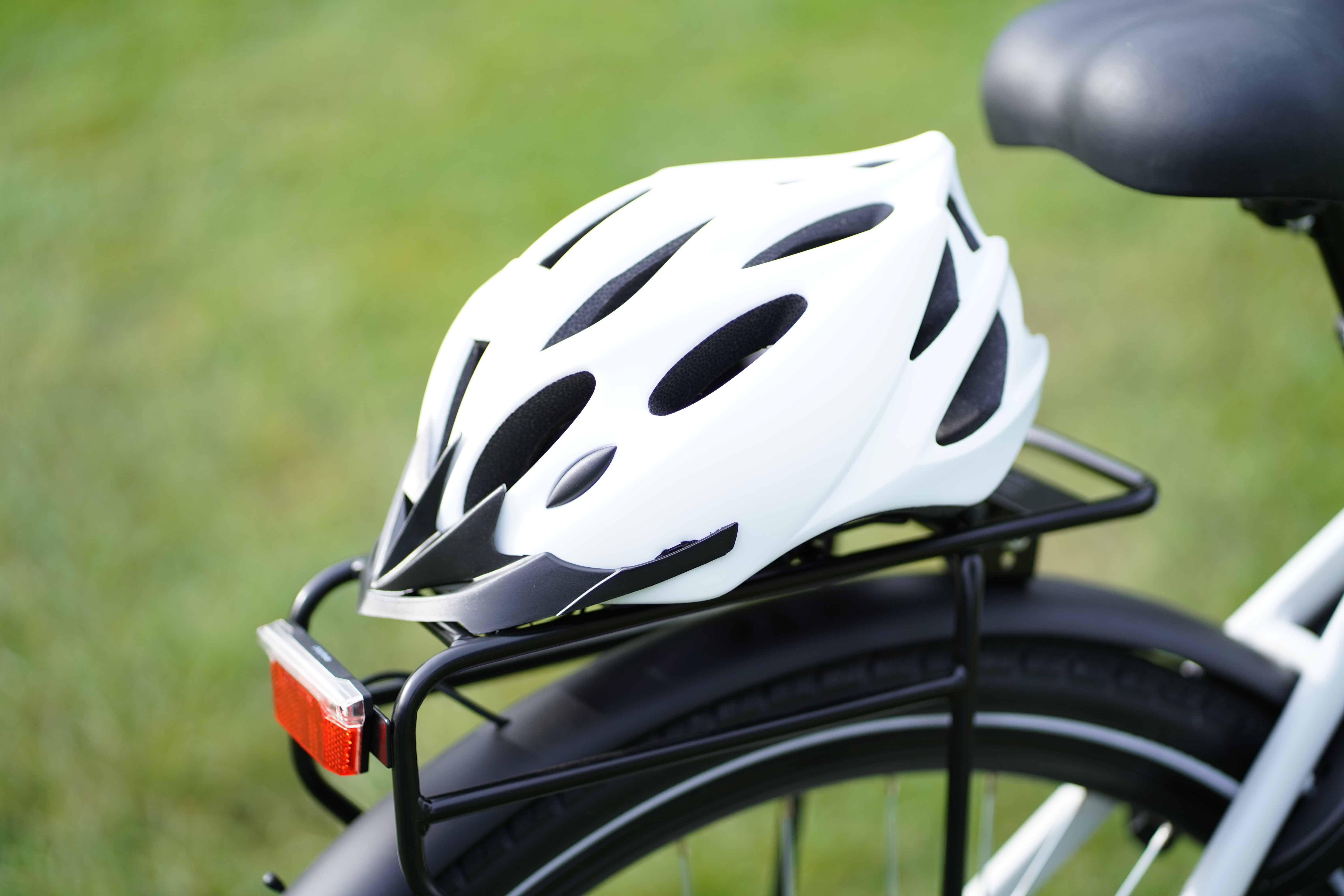 Weißer Fahrradhelm auf dem Gepäckträger eines Fahrrads vor grünem Gras.