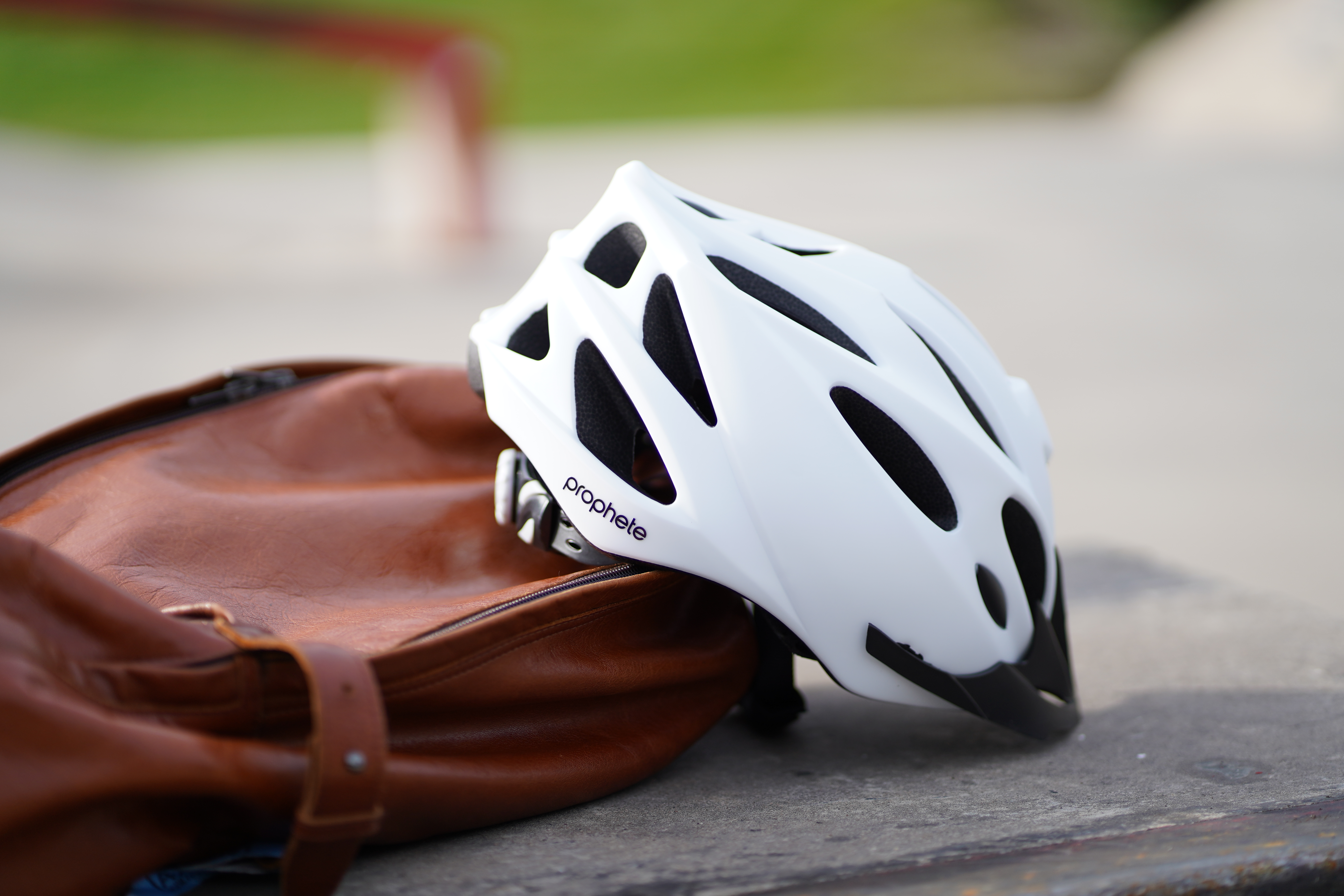 Weisser Fahrradhelm mit dem Markennamen 'Prophete', neben einer braunen Tasche auf einer Oberfläche.
