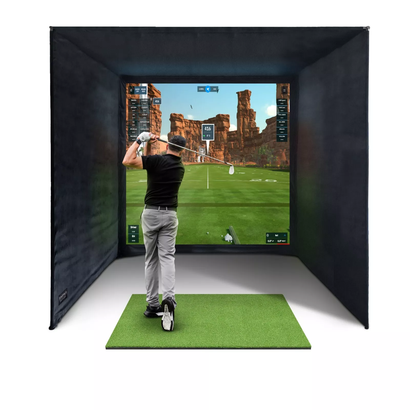 Mann spielt Golf in einem Simulatorraum, grüne Matte, digitaler Bildschirm mit Landschaft.