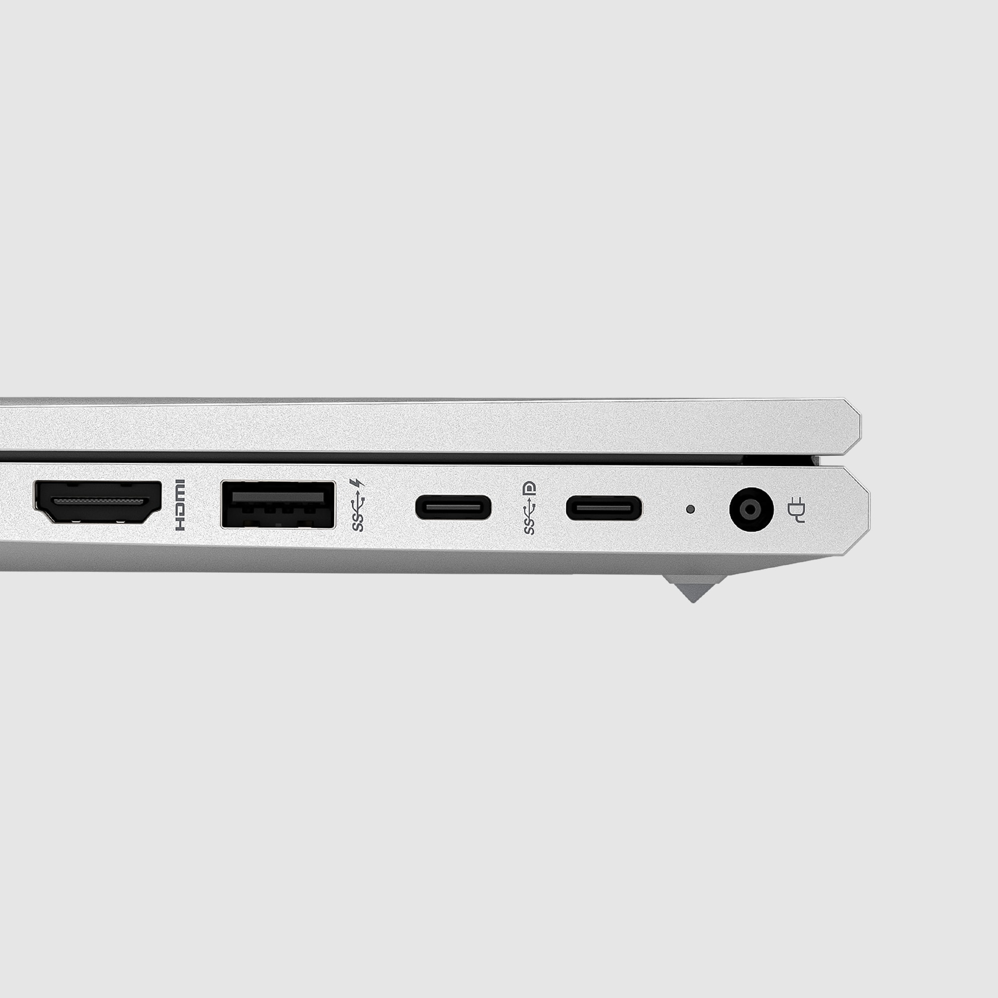 Zbliżenie na bok srebrnego laptopa pokazujące porty HDMI, USB, USB-C i port zasilania na białej powierzchni.