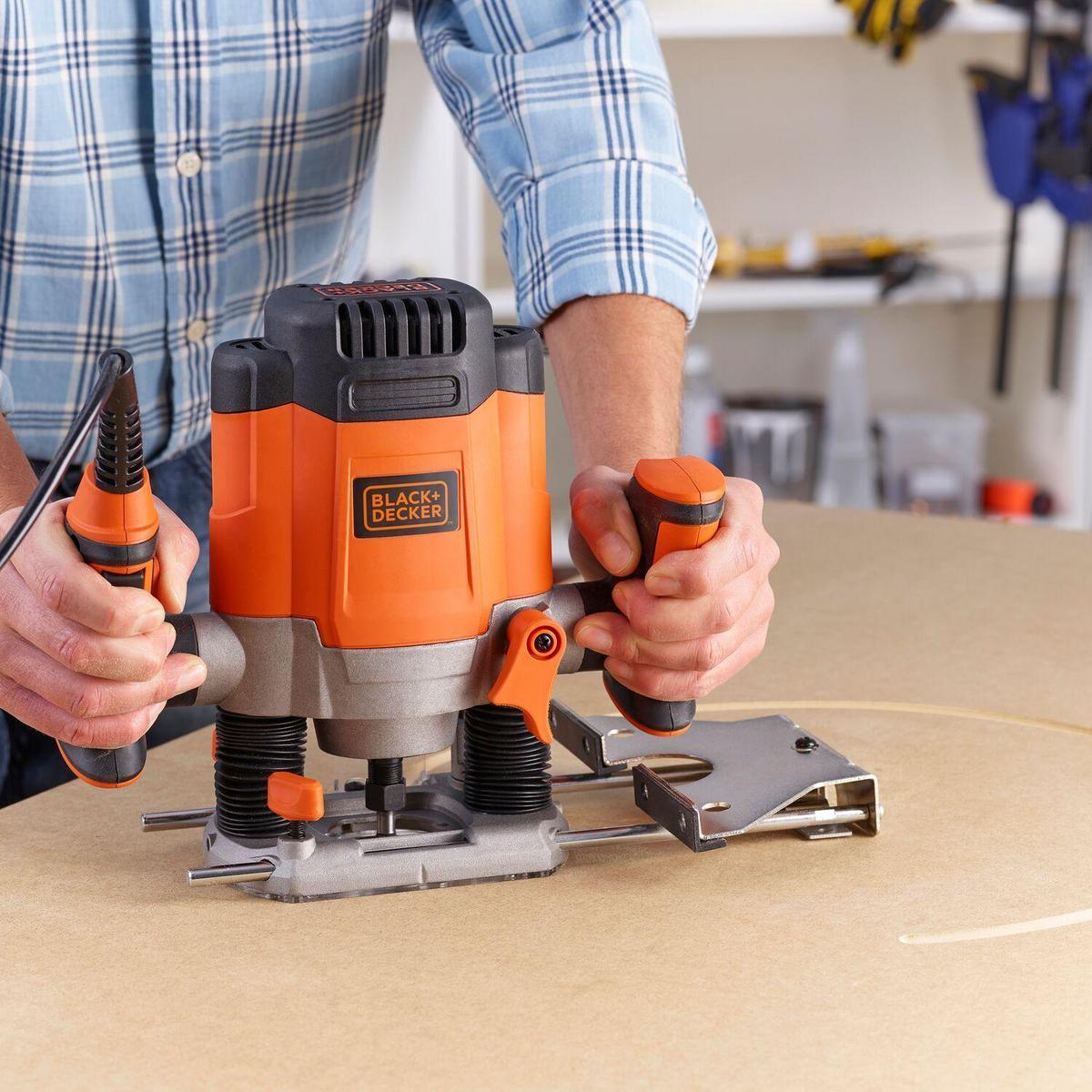 Hombre usando una herramienta de enrutador negra y naranja sobre una superficie de madera. Fondo claro.