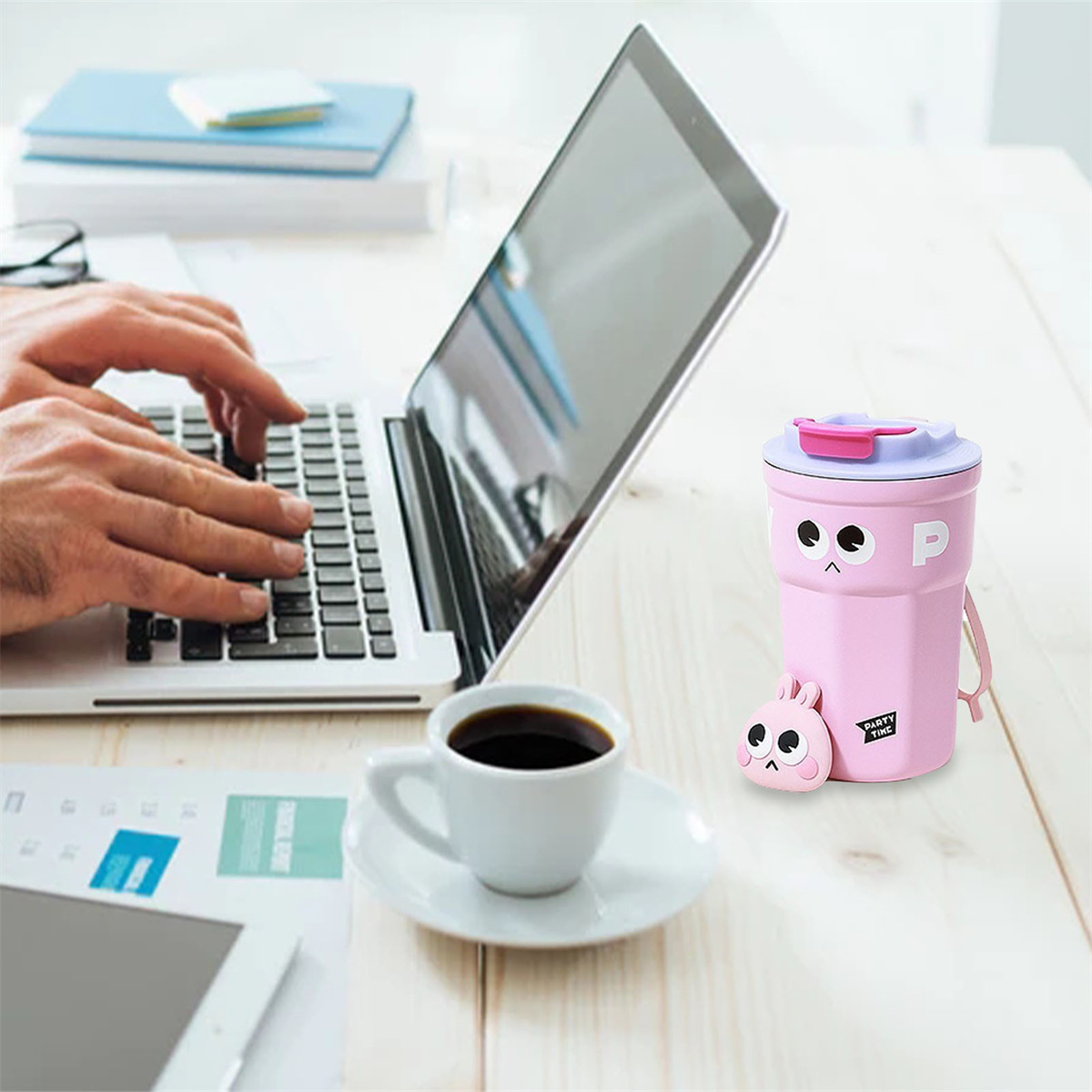 Eine Person, die auf einem Laptop tippt, mit einer Tasse Kaffee und einem rosa Becher auf dem Tisch.