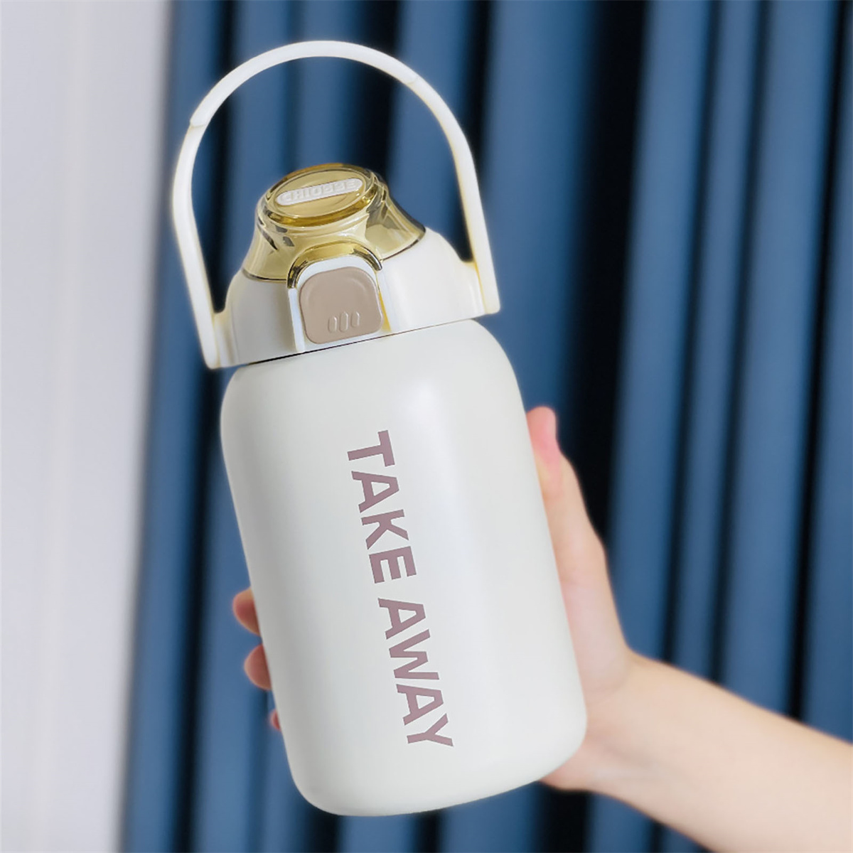 Weiße Wasserflasche, gehalten von einer Hand, mit rotem "TAKE AWAY" Text. Blauer Vorhang im Hintergrund.