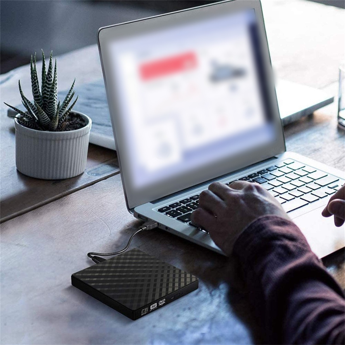 Ein Laptop mit angeschlossener externer Festplatte, platziert auf einem Holztisch mit einer Pflanze.