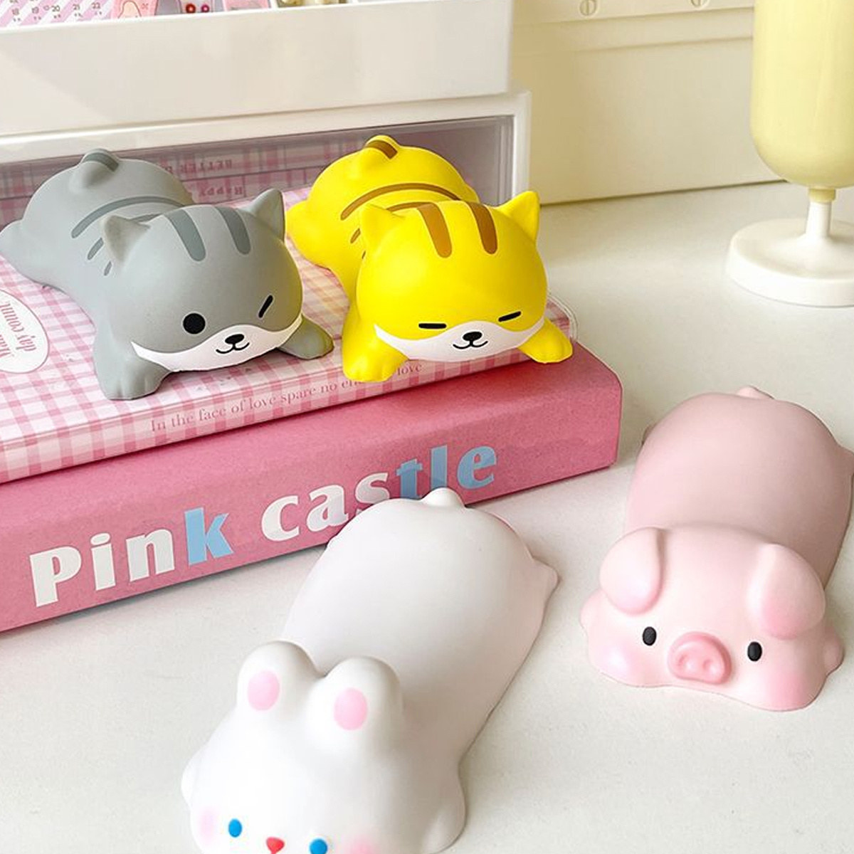 Spielzeug: Katzen und Schweine geformt, auf einem rosa Buch, weiß und gelb. Weißer Hintergrund.