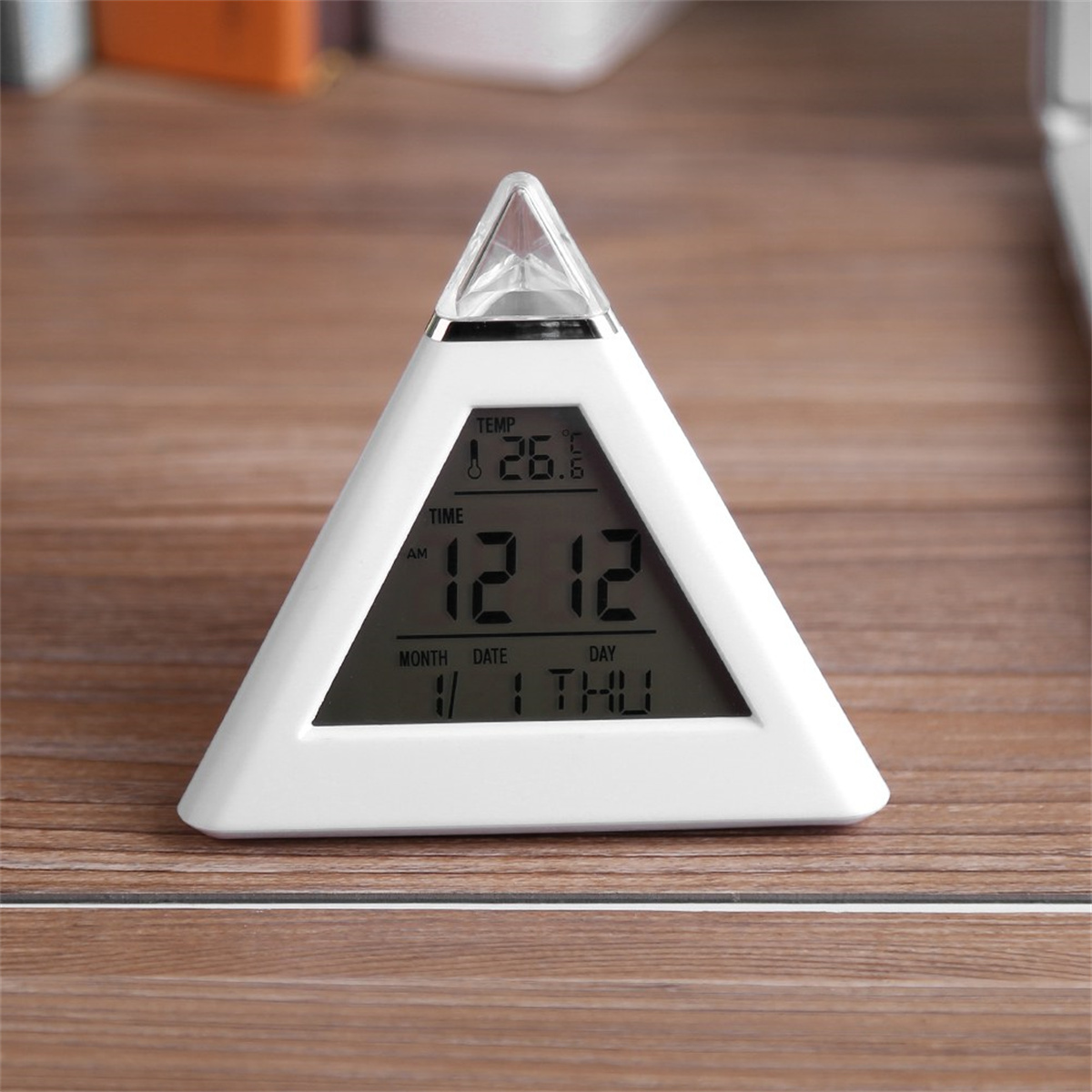 Eine weiße, dreieckige Digitaluhr, die Zeit, Datum und Temperatur auf einer Holzoberfläche anzeigt.