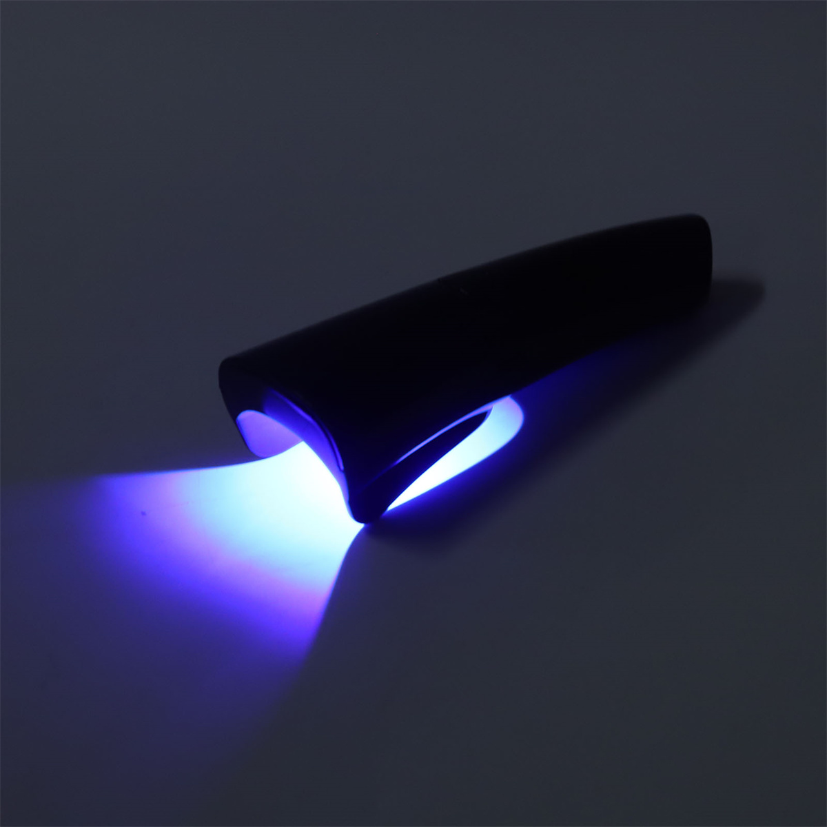 Eine schwarze, tragbare UV-Lampe, die blaues Licht aussendet. Das Licht befindet sich auf einer weißen Oberfläche.