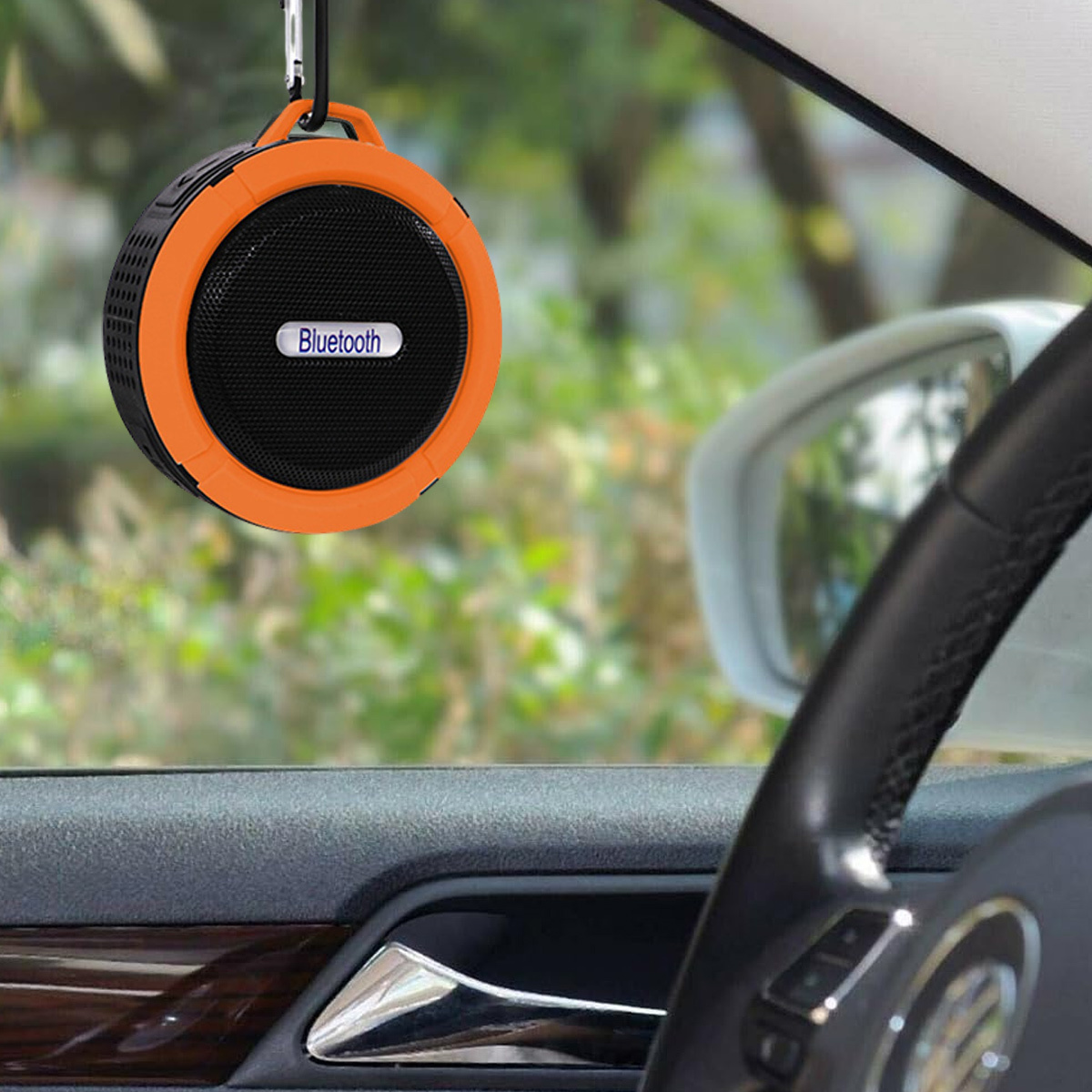 Orangener und schwarzer Bluetooth-Lautsprecher, der in einem Auto hängt. Verschwommene Grünfläche.