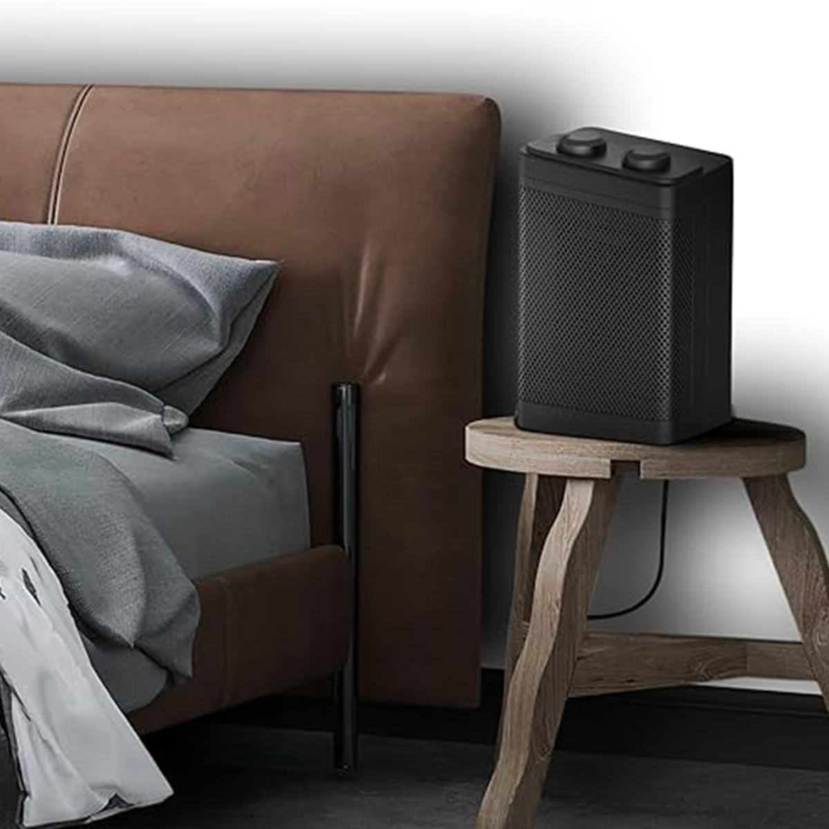 Ein schwarzer elektrischer Heizlüfter auf einem Holzschemel neben einem Bett mit braunem Kopfteil.