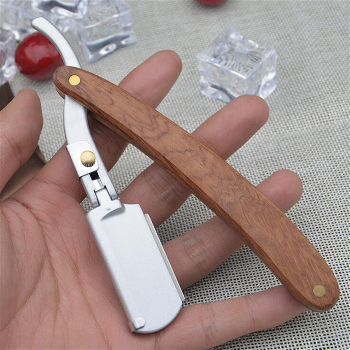 Ein gerader Rasierer mit Holzgriff in der Hand mit einer roten Kirsche und Eiswürfeln.