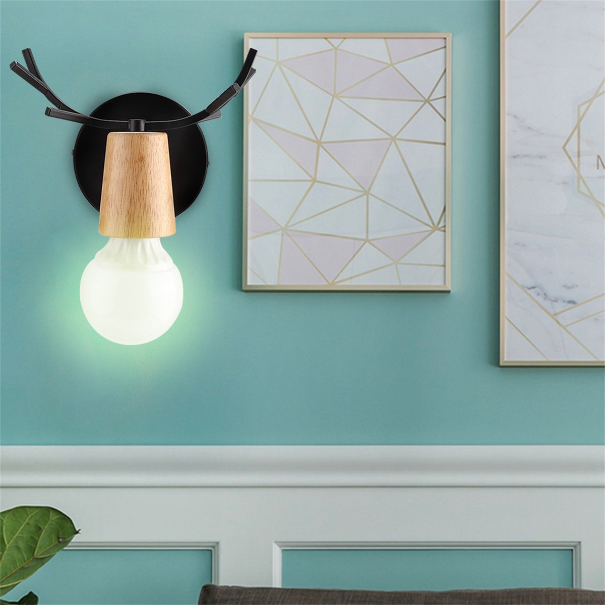 Gewei-förmige Wandlampe mit Holzakzent. Glühbirne leuchtet. Zwei gerahmte Bilder an teal Wand.