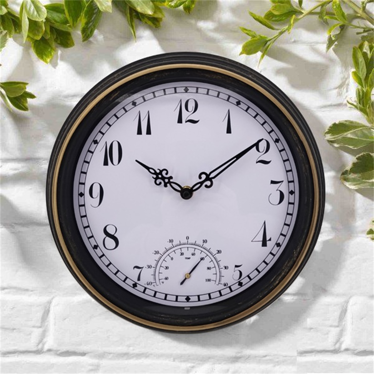 Runde schwarze Uhr mit weißem Zifferblatt, römischen Ziffern und Temperaturanzeige, an einer Ziegelmauer.