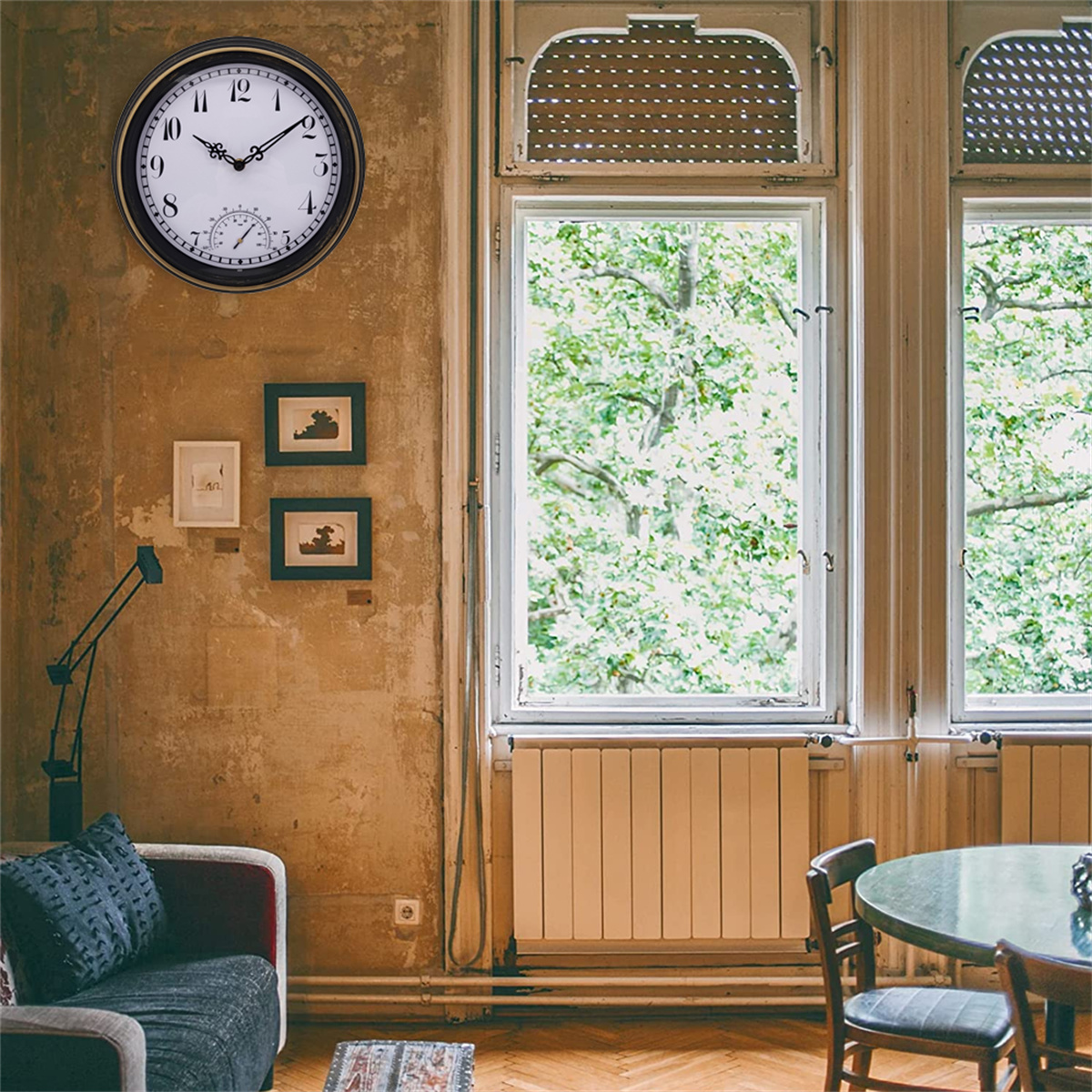 Antike Uhr an der Wand. Zwei gerahmte Bilder darunter. Fenster, Bäume draußen sichtbar. Beigefarbene Wand.
