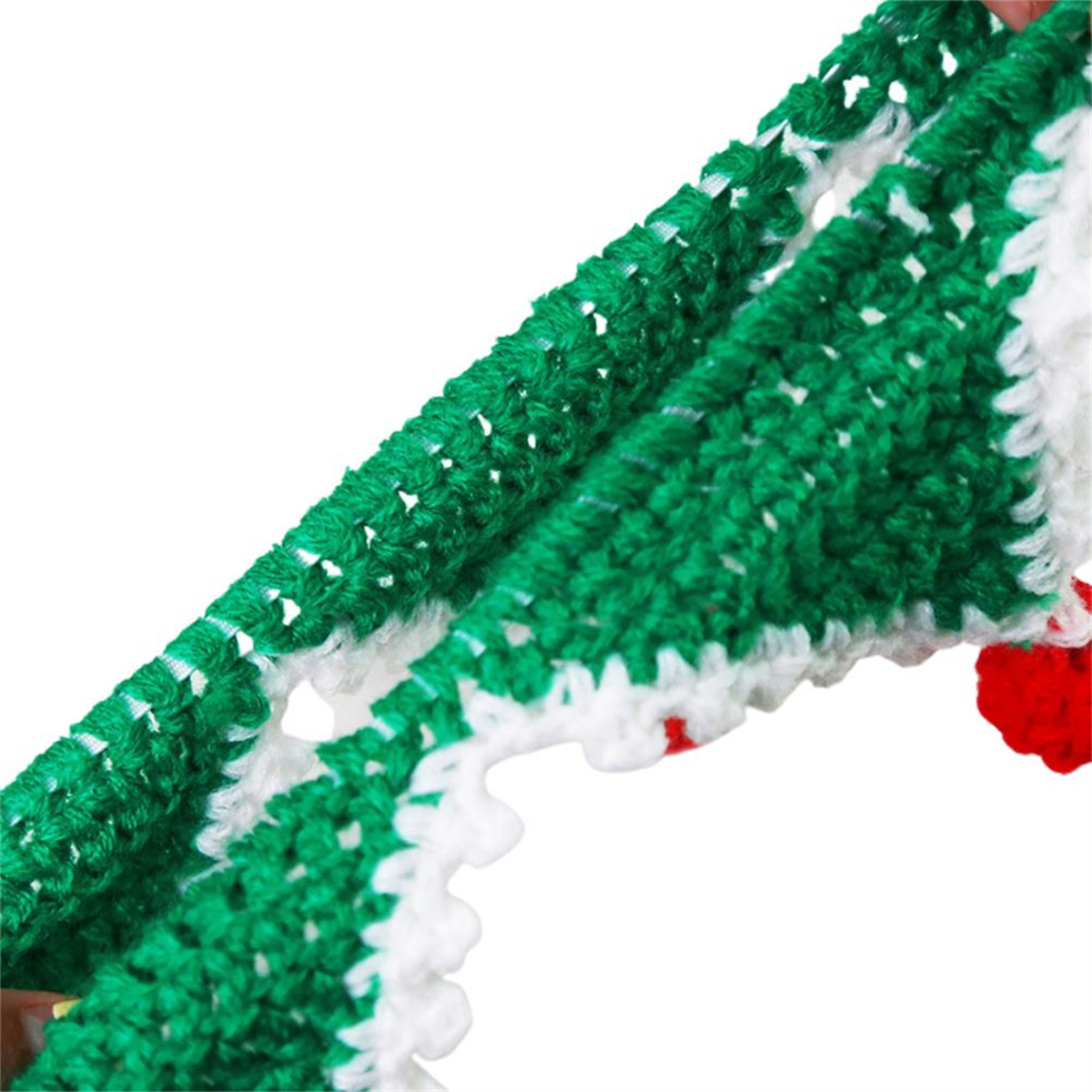 Nahaufnahme einer grün-weißen gehäkelten Weihnachtsdekoration. Rote Bommel sind ebenfalls sichtbar.