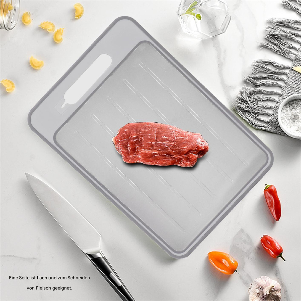 Fleisch auf einem grauen Tablett mit einem Messer und Gemüse, das Tablett hat einen Griff.
