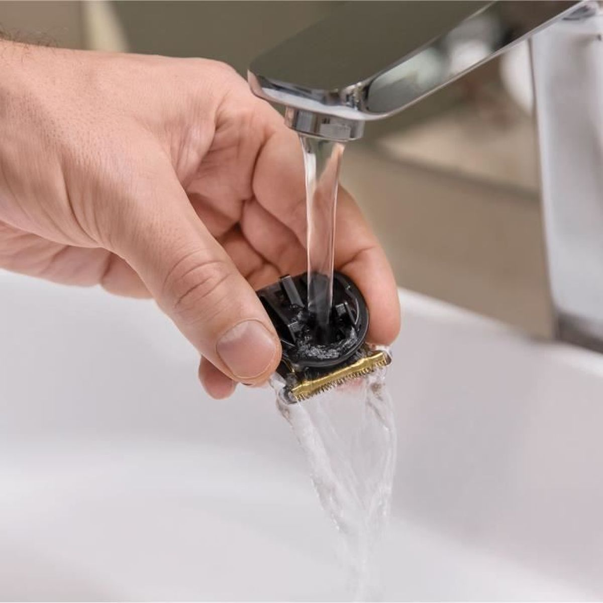 Hand hält einen schwarzen Trimmer unter fließendem Wasser in einem weißen Waschbecken.