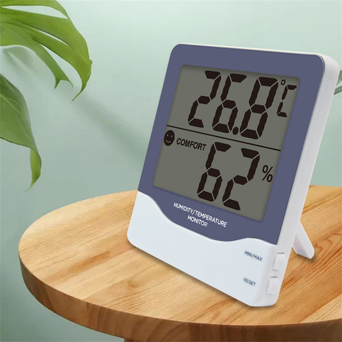 Digitales Feuchtigkeits-/Temperaturmessgerät zeigt 26,8 °C und 62 % an. Es steht auf einem Holztisch mit einer grünen Pflanze.