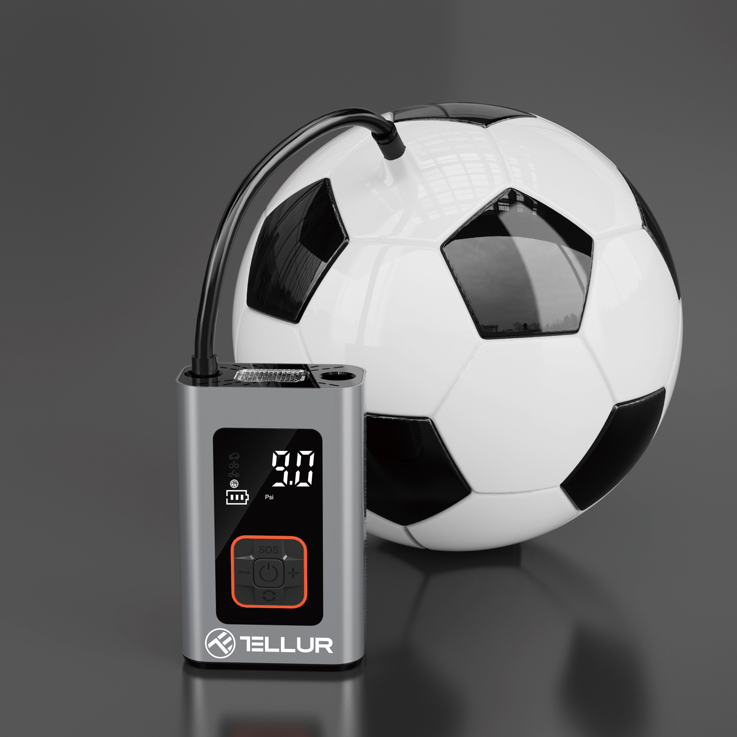 Piłka nożna obok srebrno-czarnej pompki powietrza, na ciemnej powierzchni.