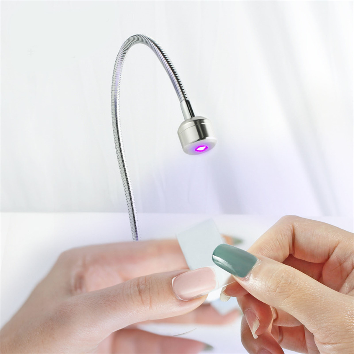Eine Nagellampe mit flexiblem Hals. Die Hände einer Person zeigen eine Maniküre mit einem grünen und rosa Nagel.