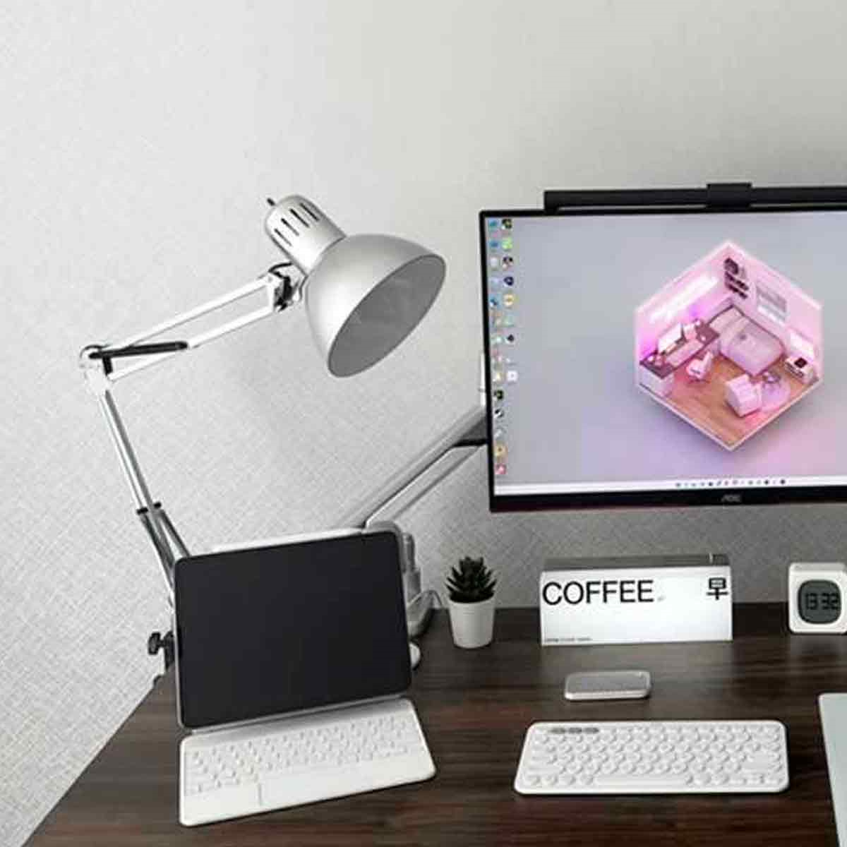 Ein Schreibtisch-Setup mit einer silbernen Lampe, Tablet, Tastatur, Monitor und Kaffeetasse.