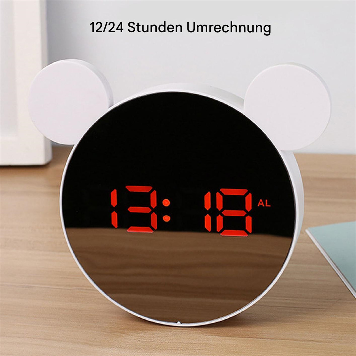 Ein weißer, bärenförmiger digitaler Wecker zeigt 13:18 an. Der Hintergrund ist ein Tisch.