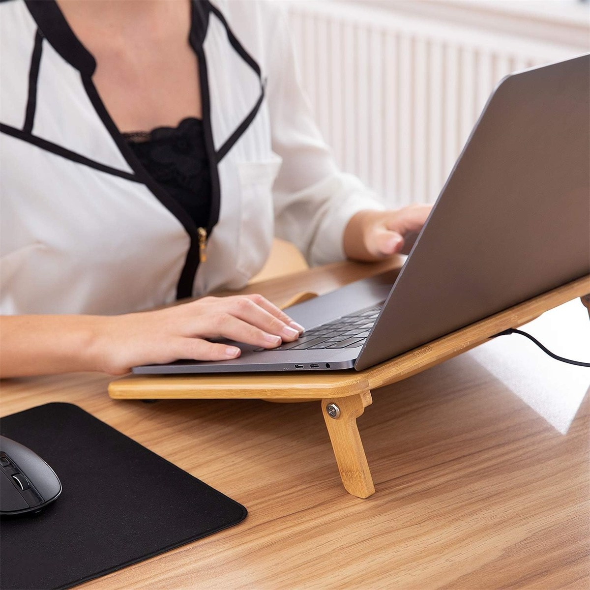 Ein Laptop auf einem Holzständer auf einem Schreibtisch. Eine Maus und ein Mauspad befinden sich links.