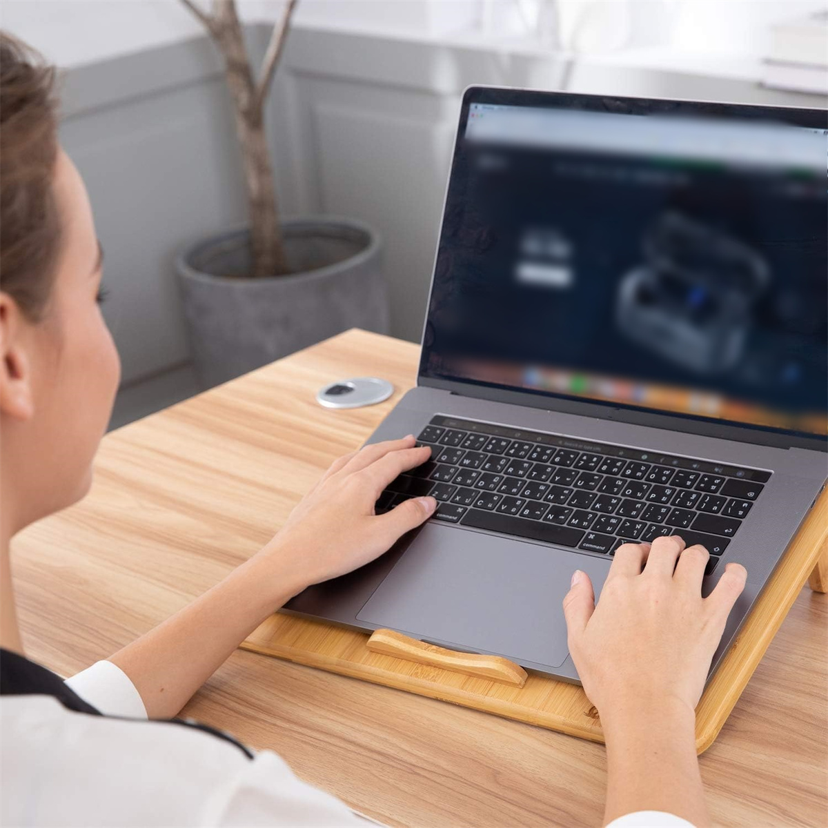 Frau benutzt einen Laptop auf einem Holzschreibtisch mit Laptopständer.