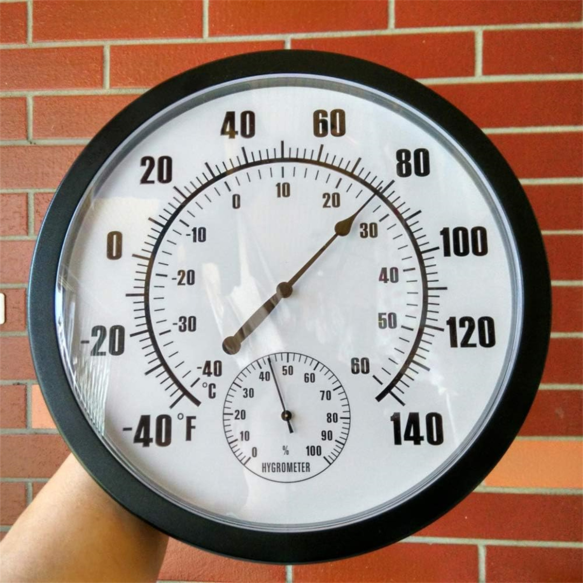 Ein runder Thermometer und Hygrometer mit schwarzem Rahmen und weißem Hintergrund, der Temperatur und Feuchtigkeit anzeigt.