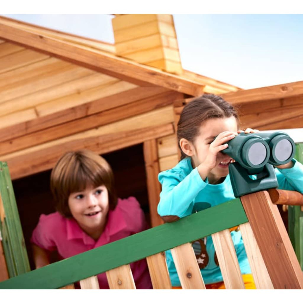 Zwei Kinder in einem Holzspielhaus, eines schaut durch ein Fernglas.
