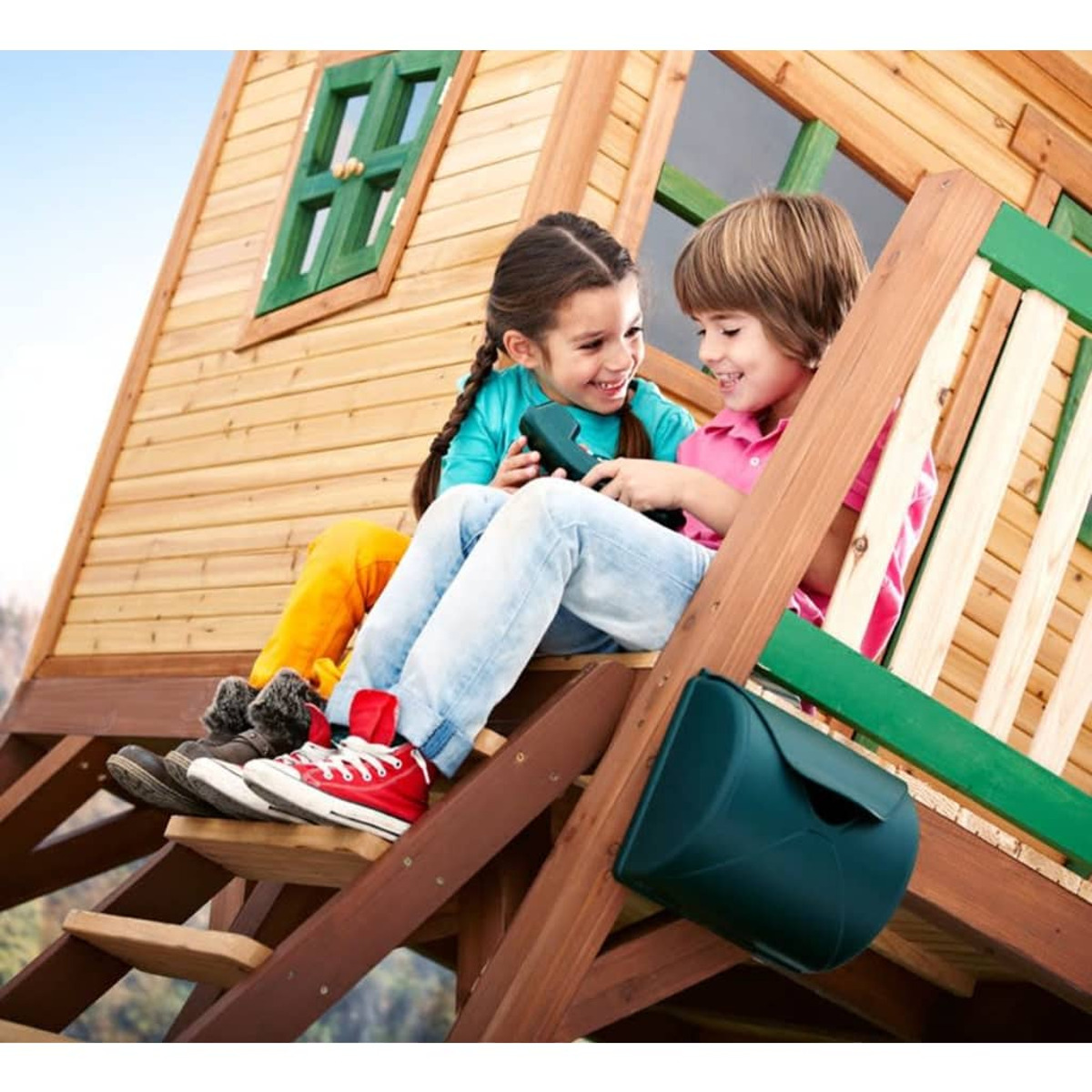 Zwei Kinder sitzen in einem hölzernen Spielhaus, lächeln und schauen sich an.